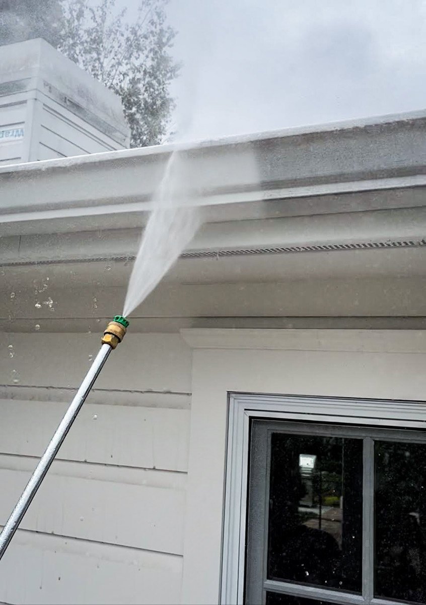 Pressure washing a white house gutter with a high-pressure water spray.