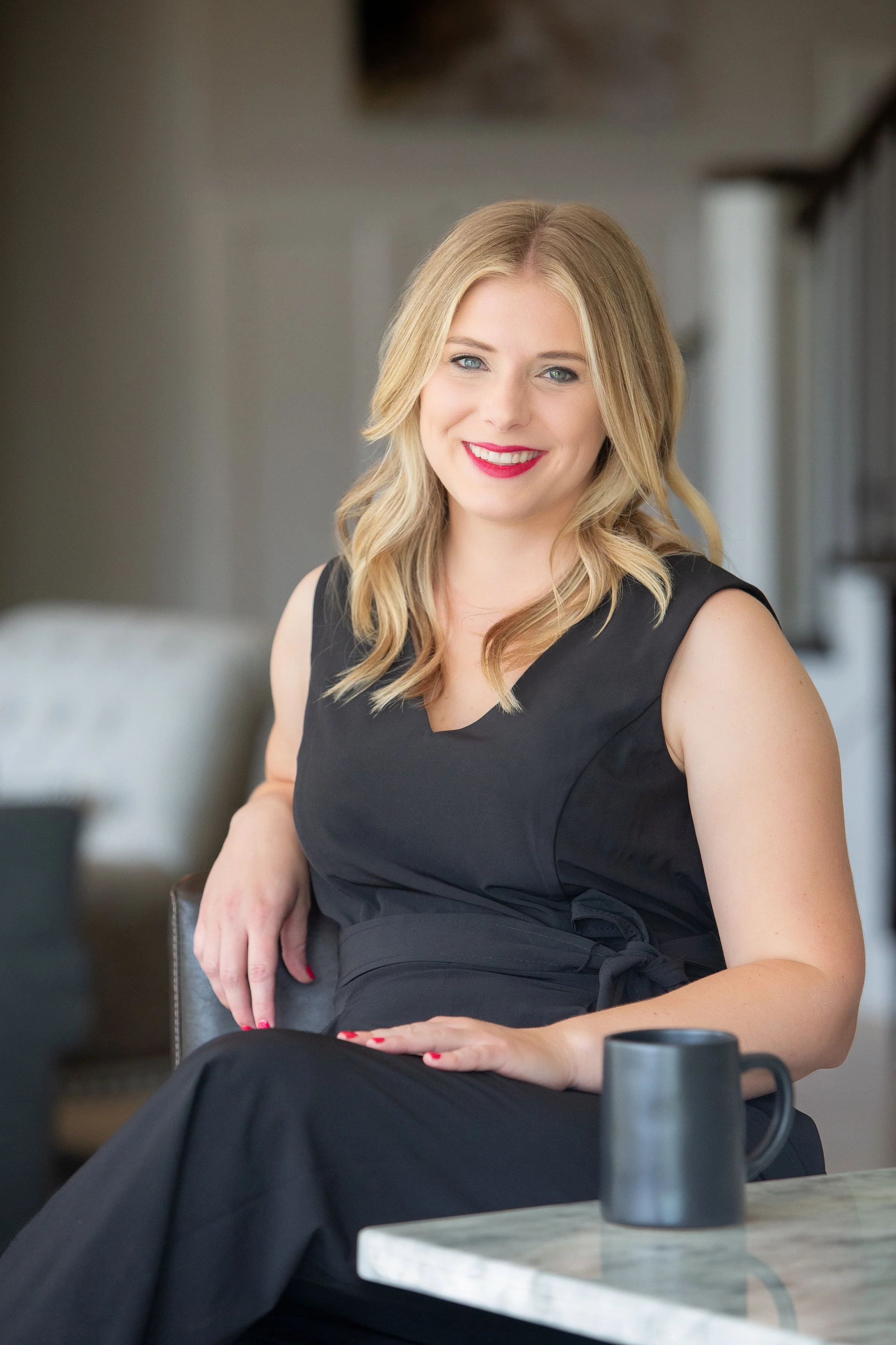 Image of blonde, white woman in a black dress, in foreground of a living room photo.