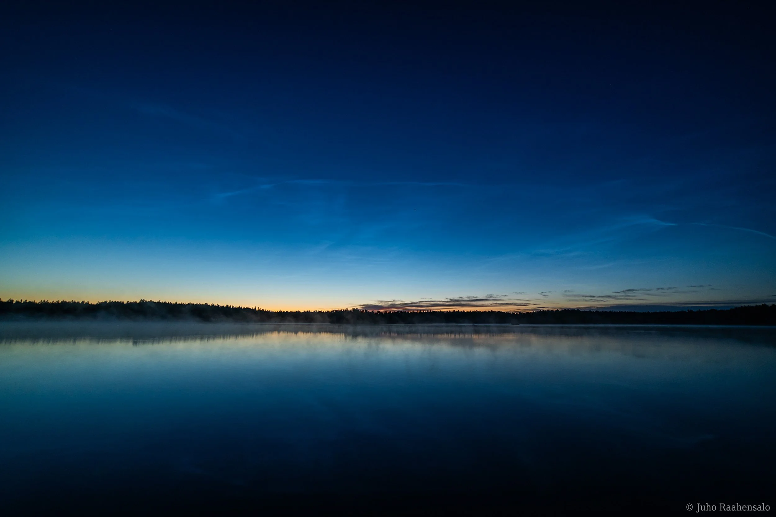 Noctilucent clouds over misty calm lake