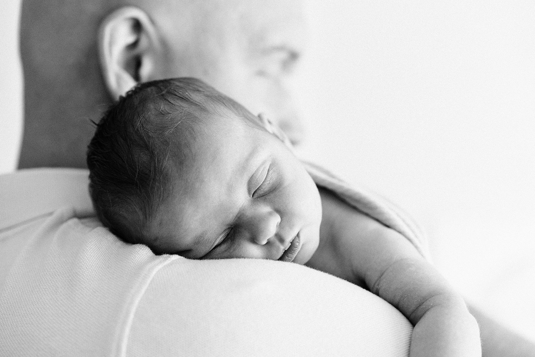 A sleeping newborn baby resting on an adult's arm, both visible in a close-up black-and-white photograph.