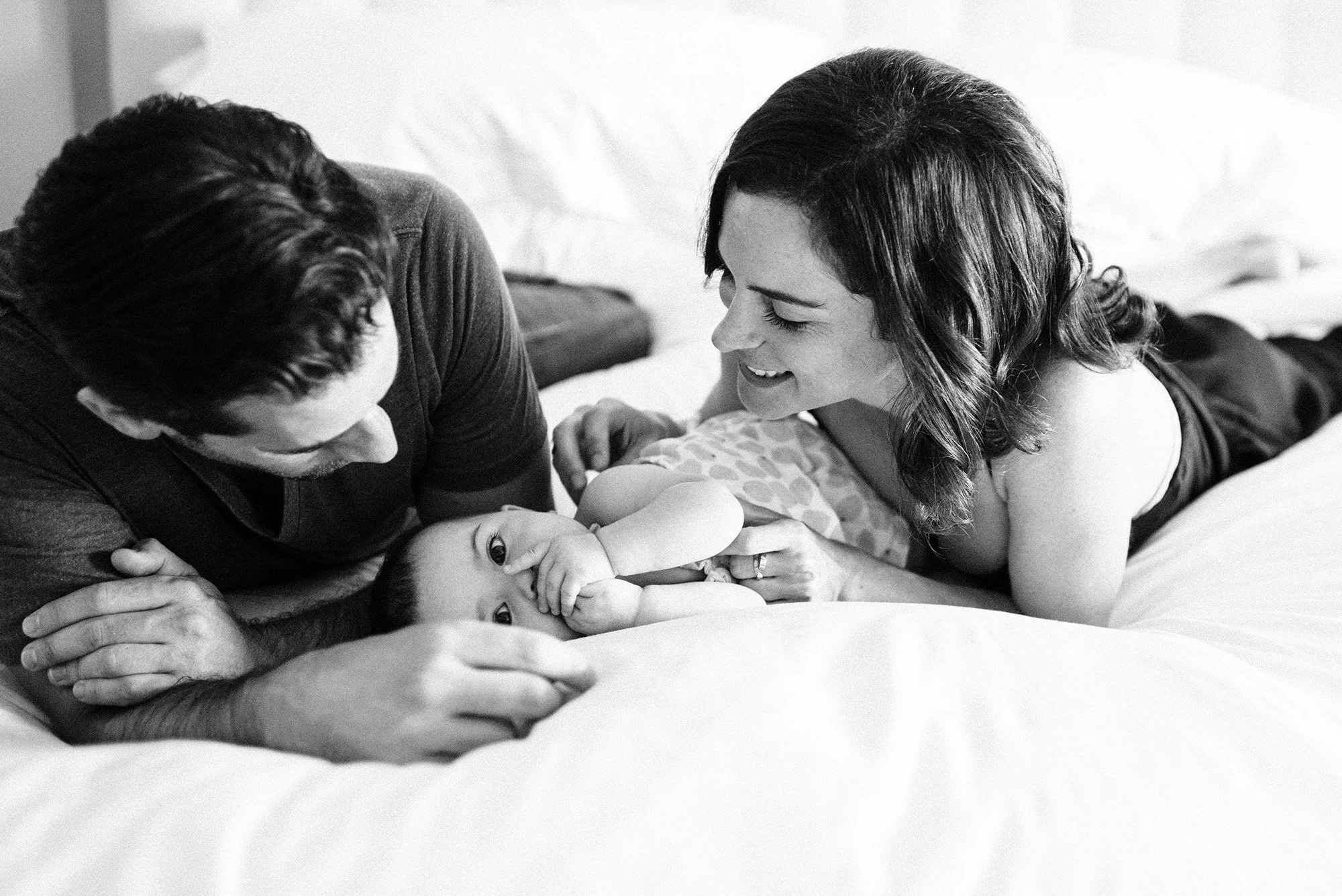 Mom dad and baby on bed playing during family photos