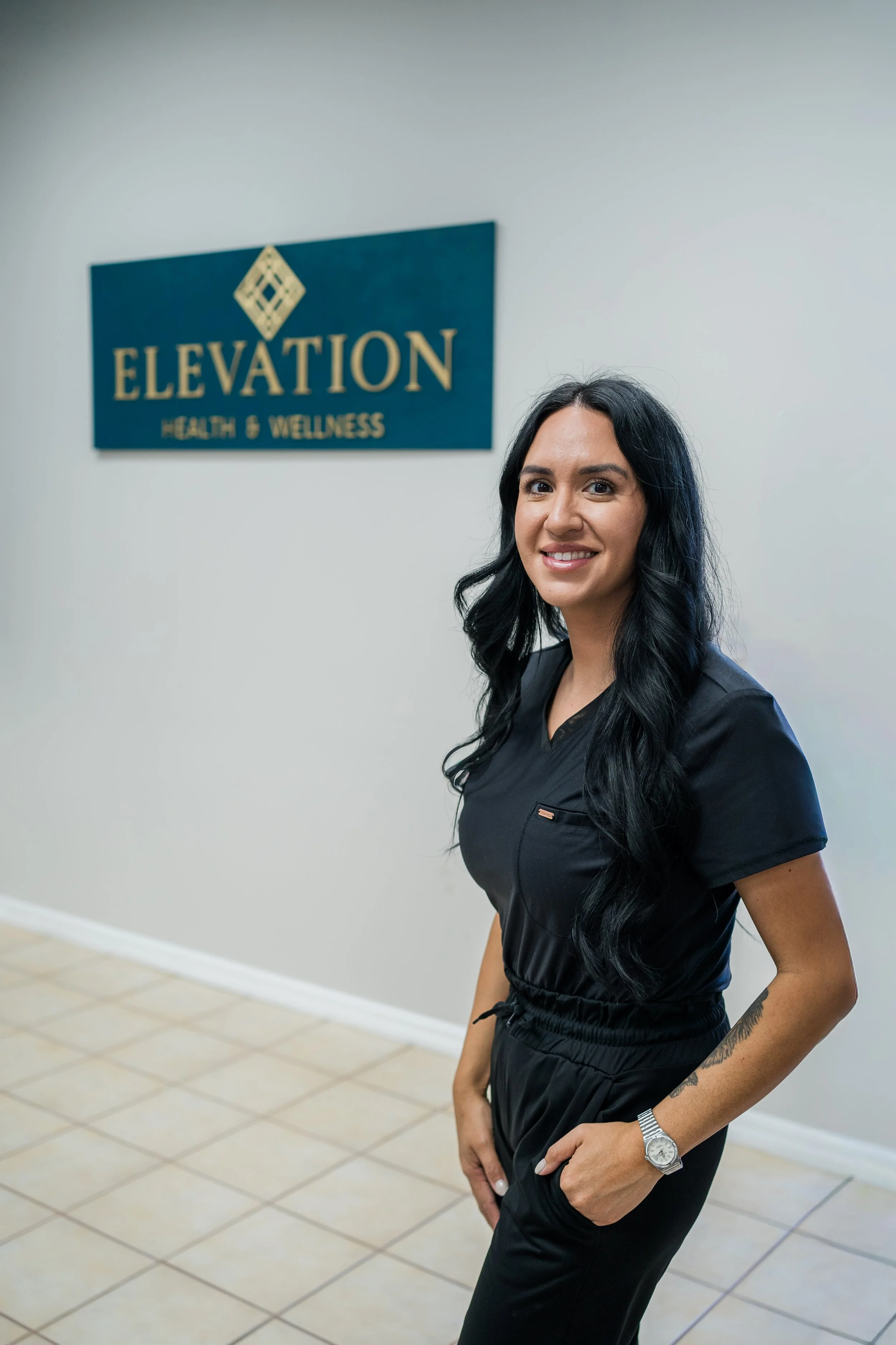 A man and woman standing back-to-back against a plain white background, both wearing dark gray scrubs and smiling at the camera.