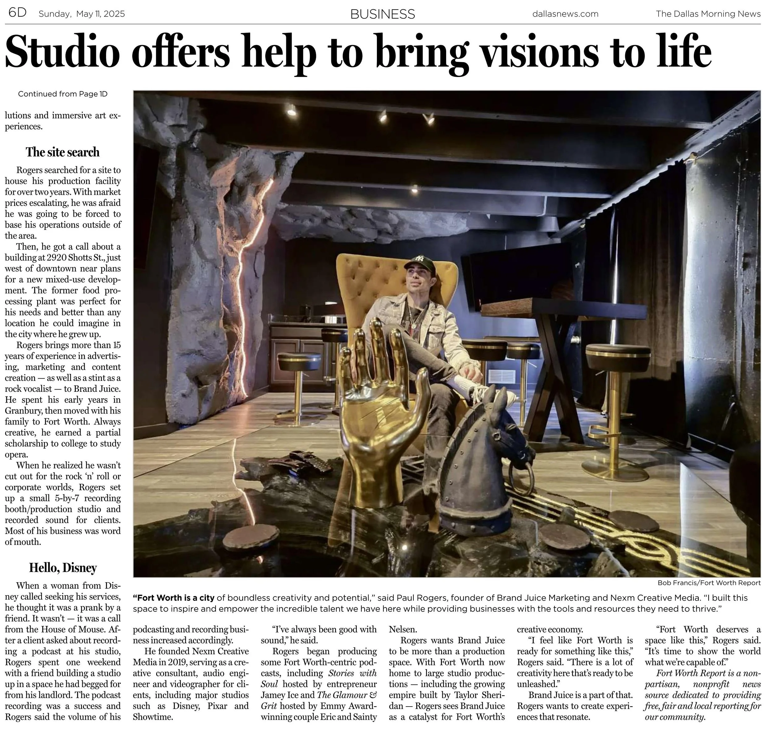 A man sitting in a modern, artistic room with creative decor, including a large gold hand sculpture, a high-backed yellow chair, and various furniture and lighting. The room features a rock wall and dark curtains.