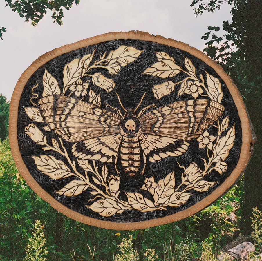 Day 3 ➖Wings 🦋
A death&rsquo;s head moth over a bed of belladonna 💀
I am running out of things to say!! I never post this much! 
&bull;
&bull;
&bull;
&bull;
&bull;
#illustration #smallbusiness #woodburning #pyrography #woodburningart #cursedrelics2