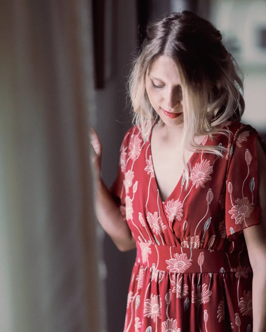A woman with blonde and black hair in a floral red dress looking downward.