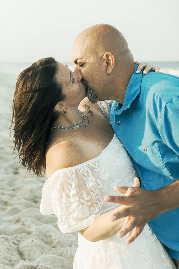 A couple sharing a kiss on the beach, with the ocean in the background.