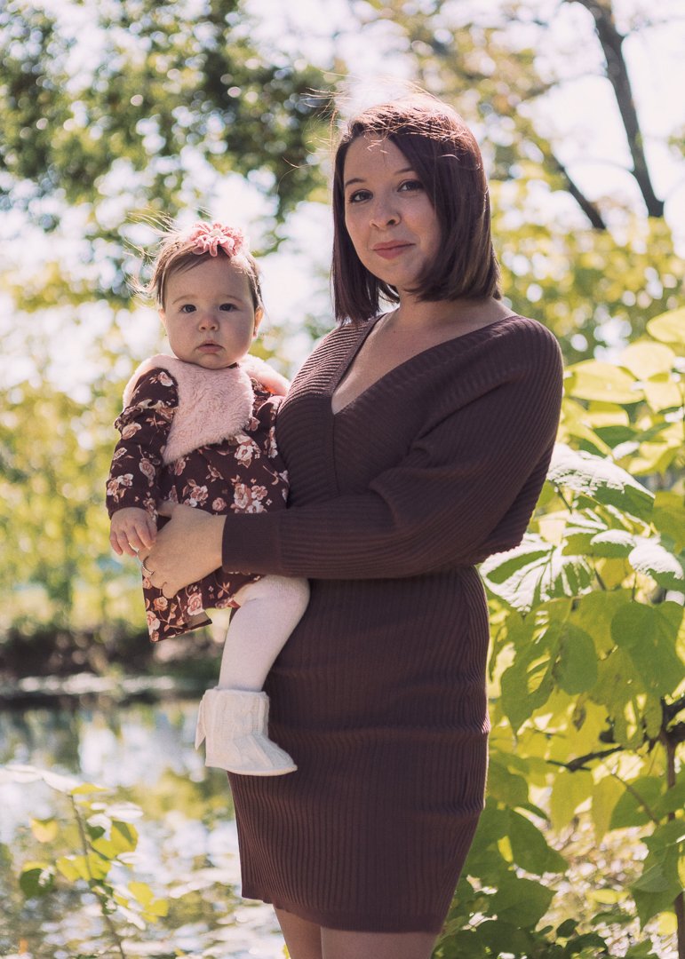 A woman holding a young girl outdoors surrounded by green leaves and sunlight.