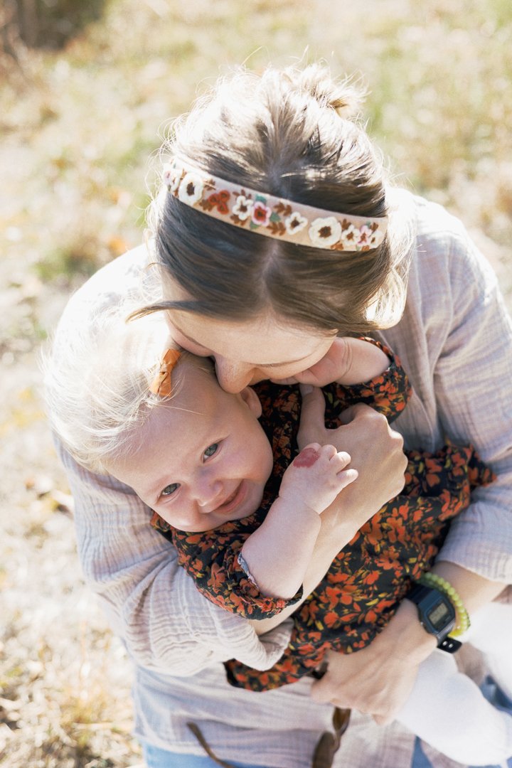 A woman hugging a smiling young girl outdoors on a sunny day.