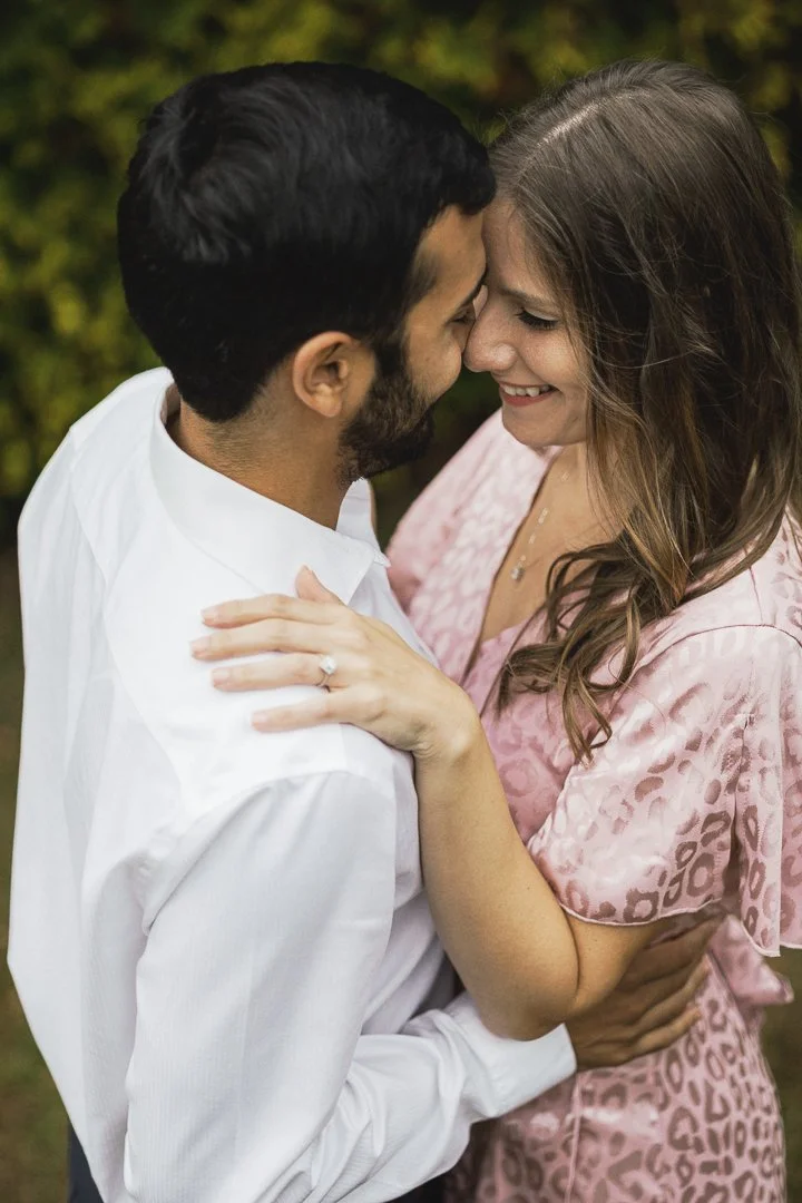 A happy couple embracing and smiling at each other outdoors, with a blurred green background.
