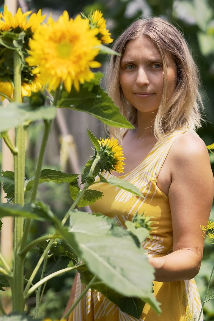 A woman in a yellow striped dress standing among sunflowers in a garden or field.