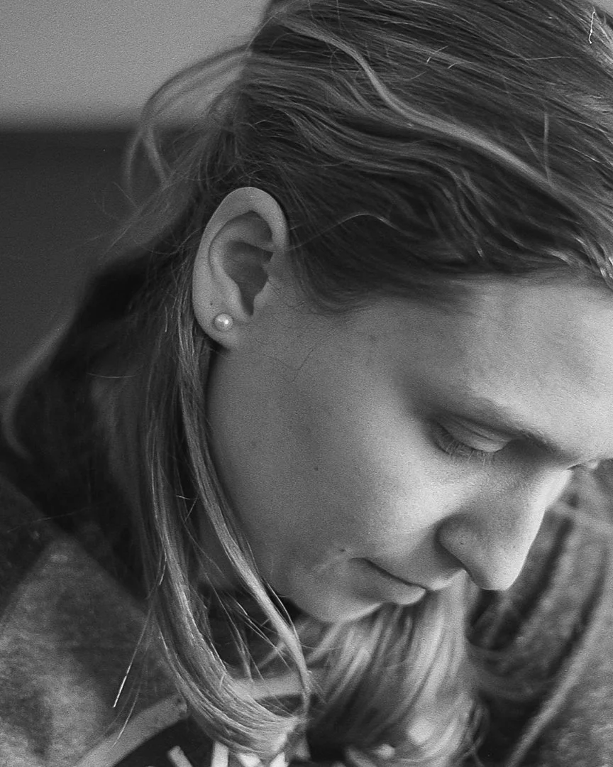 Black and white close-up of a woman with light-colored hair and small stud earring, looking downward with her eyes closed.