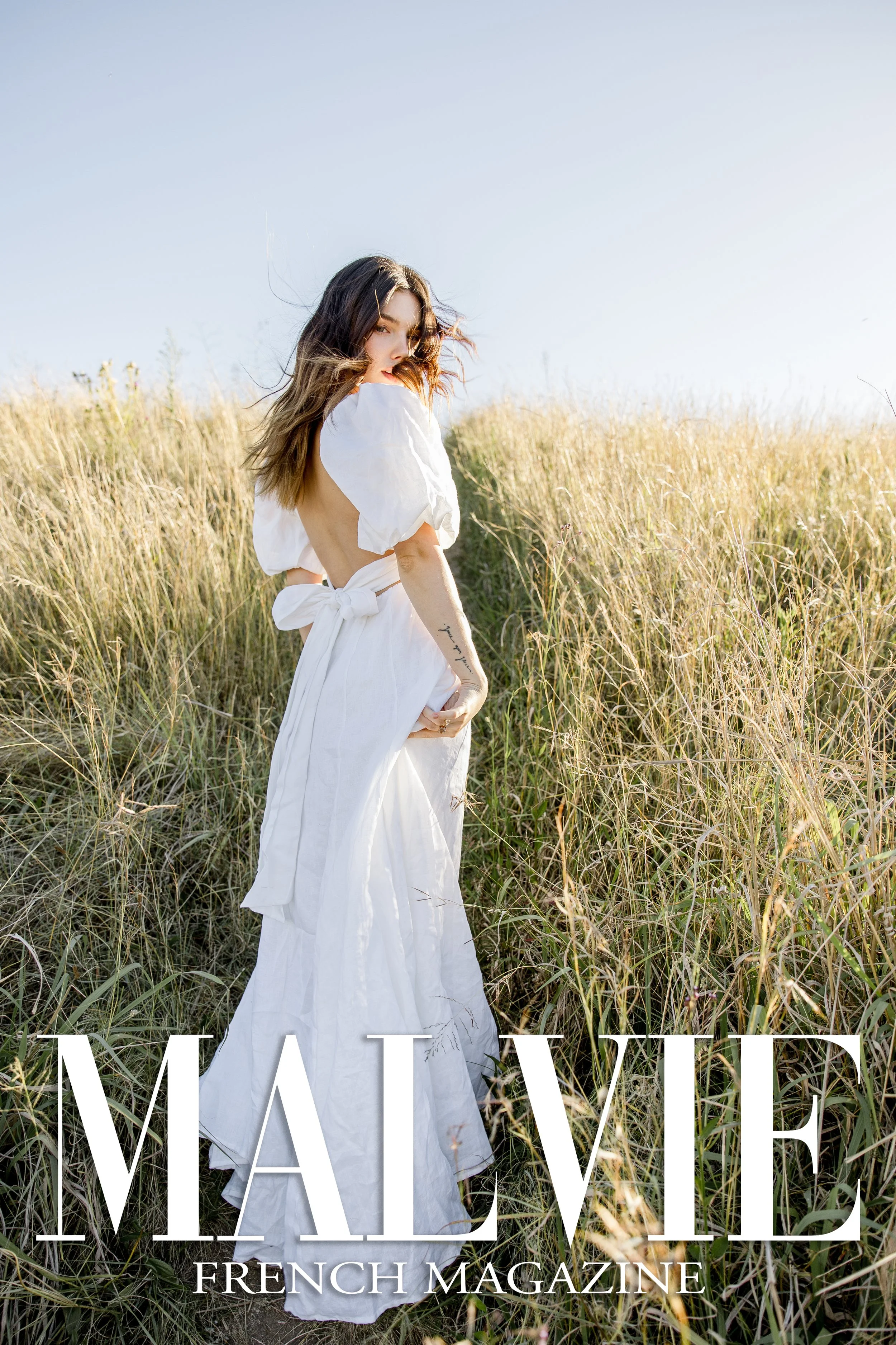A woman in a white dress standing in a field of tall grass with the words 'MALVIE FRENCH MAGAZINE' overlaid at the bottom.