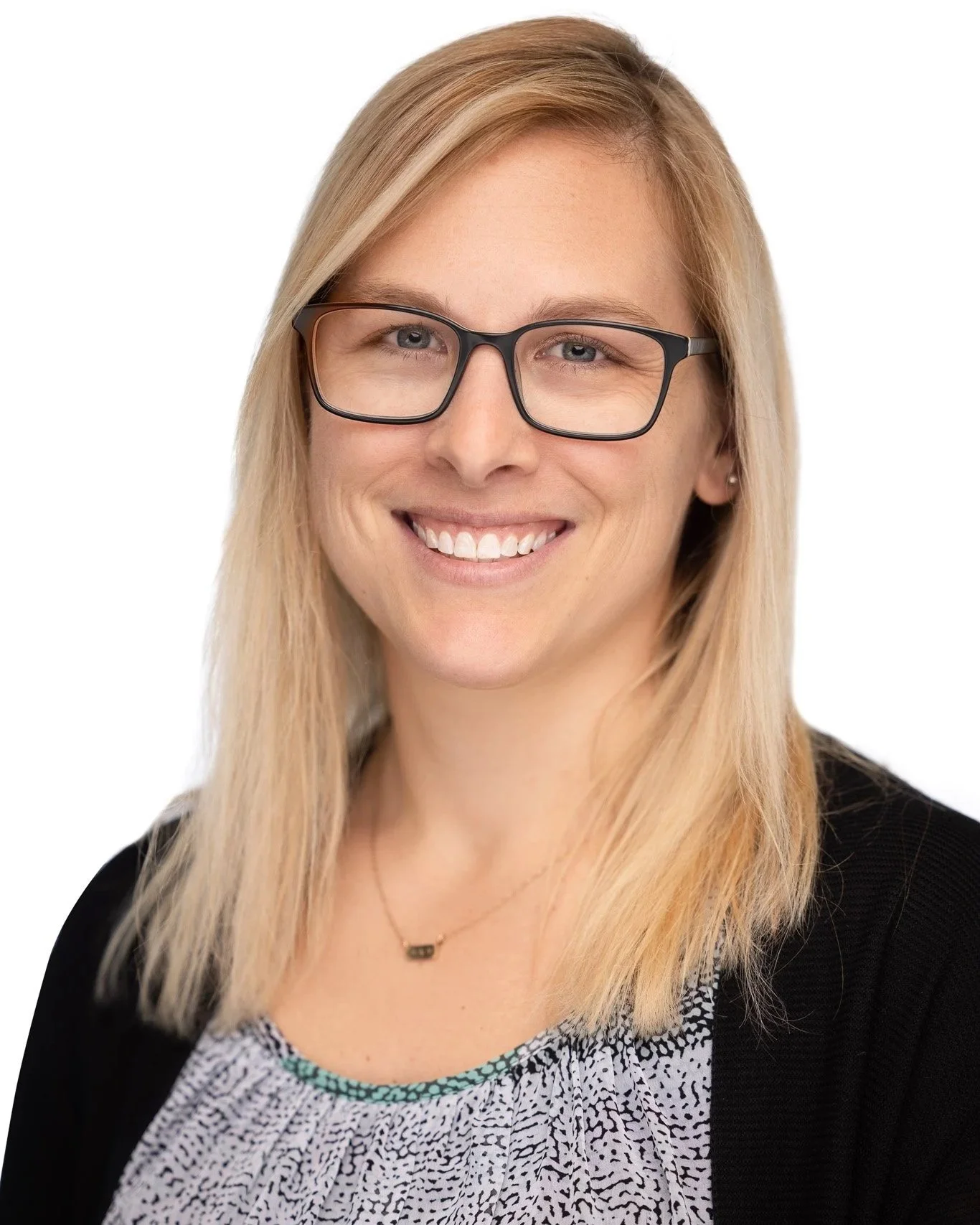 A woman with blonde hair, wearing glasses, smiling, in a black cardigan and patterned top, against a white background.