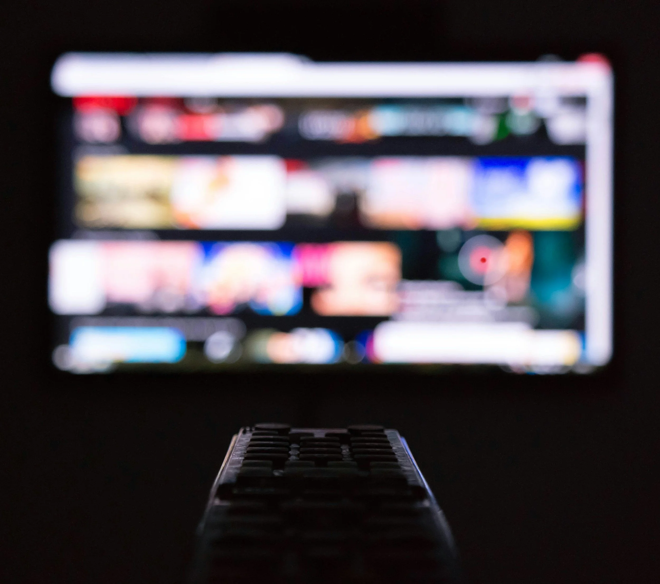 Person holding a remote control while preparing to stream content on a television in the background.