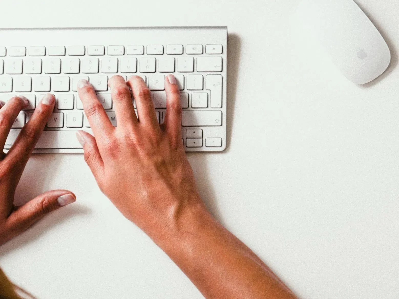 Overhead view of a person typing on a white keyboard with a mouse on a desk