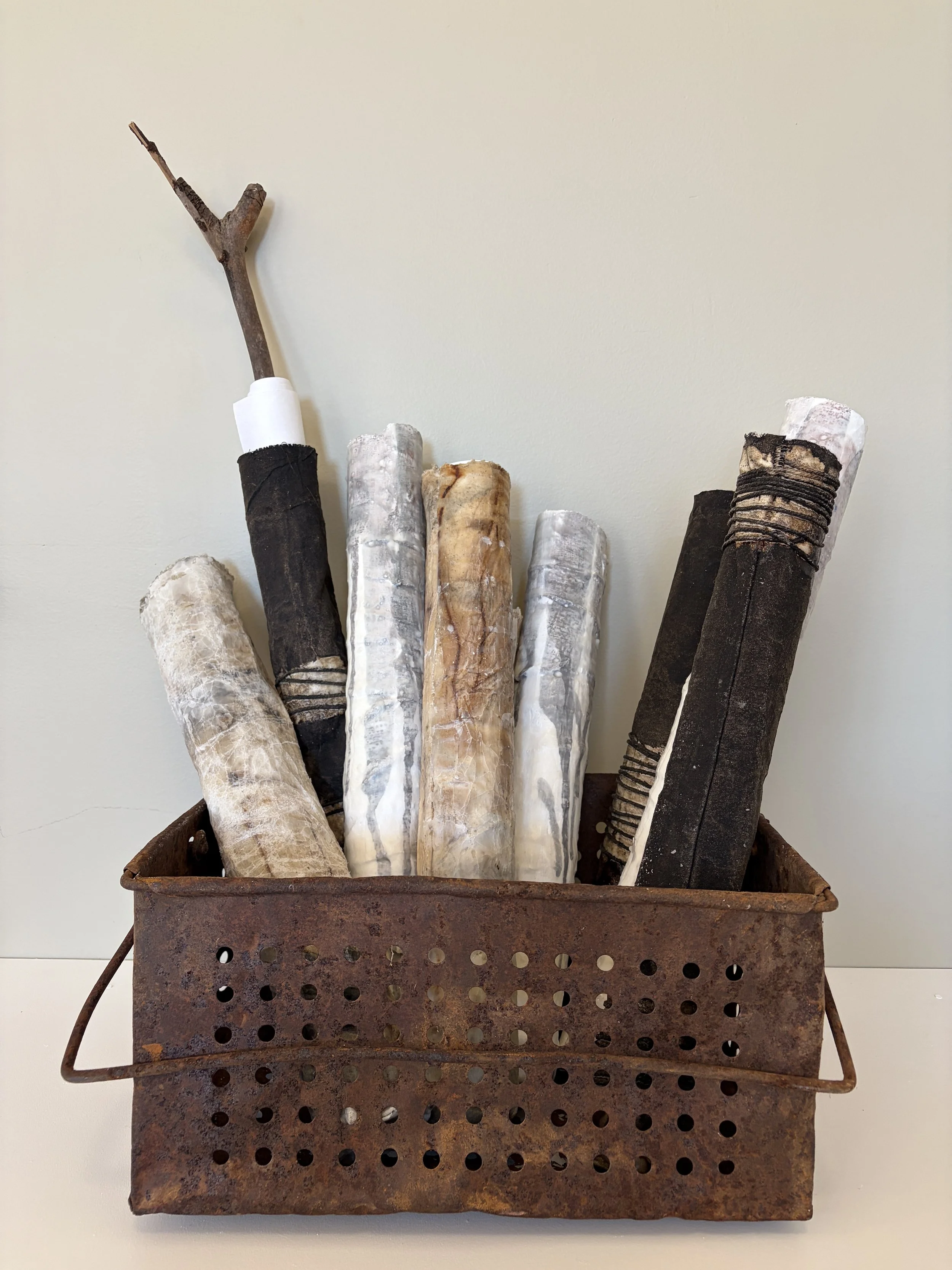 Meditation Scrolls brings together a collection of hand-worked scrolls, gathered in an old rusted basket. Layered papers, cloth, wax, stitching and binding conceal words and images within. Rolled and held rather than conventionally read, each scroll 
