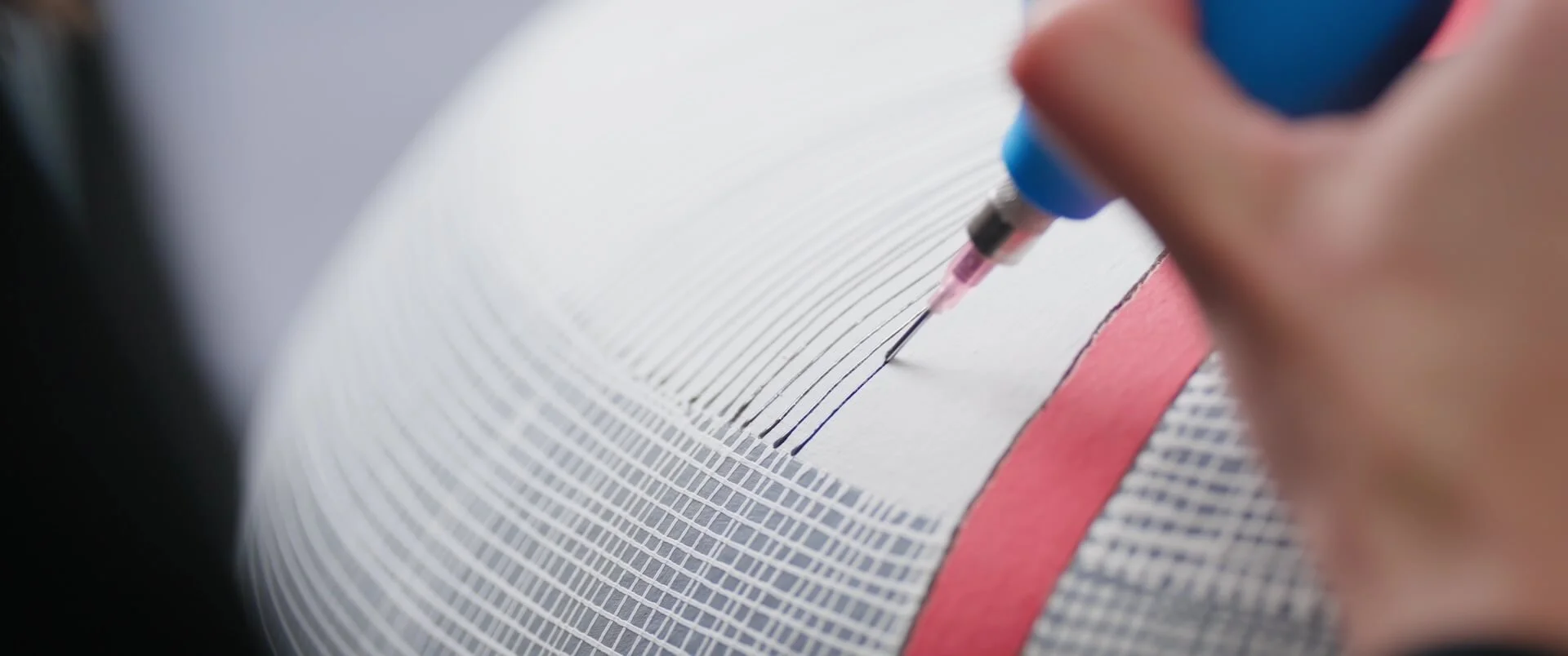 Close-up of a person's hand using a mechanical pencil to write on a graph paper notebook with a red elastic band.