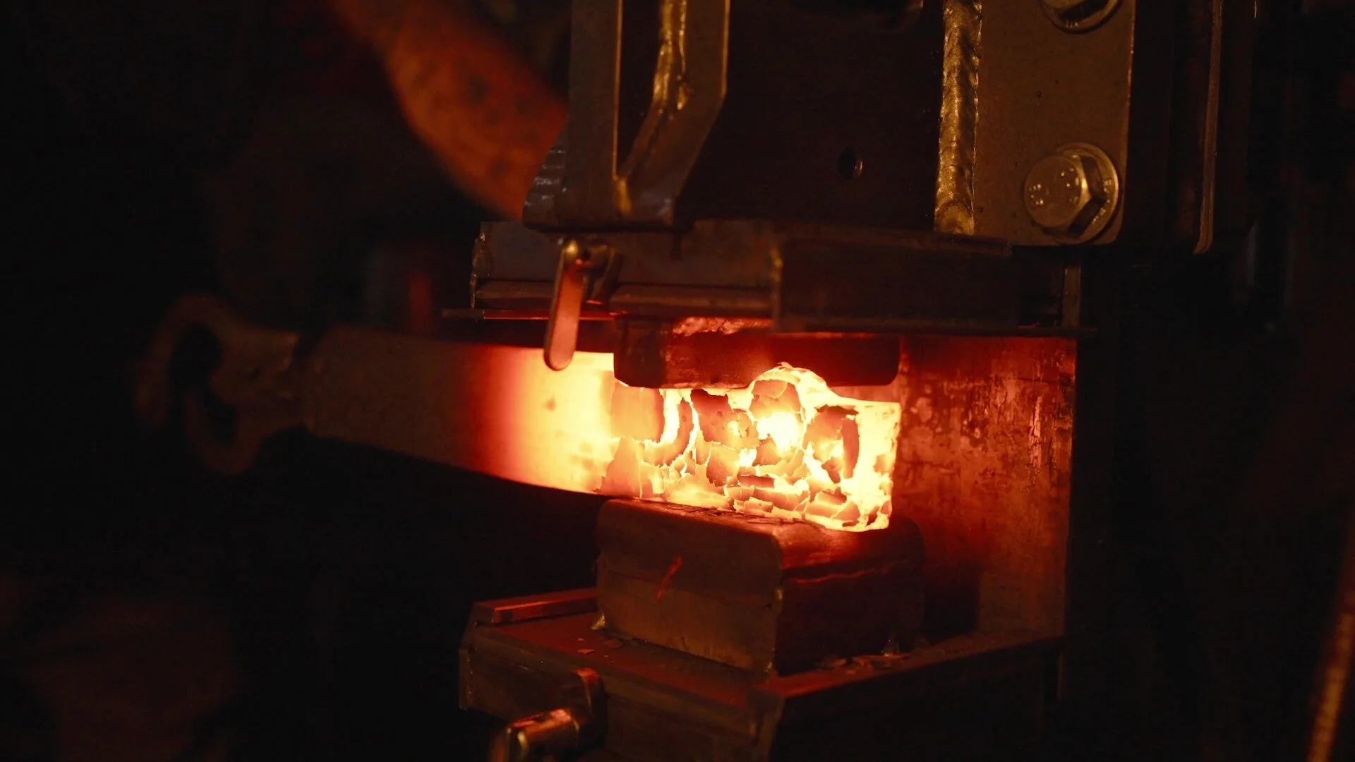 A blacksmith welding a piece of metal in a forge with bright orange flames and glowing hot metal.