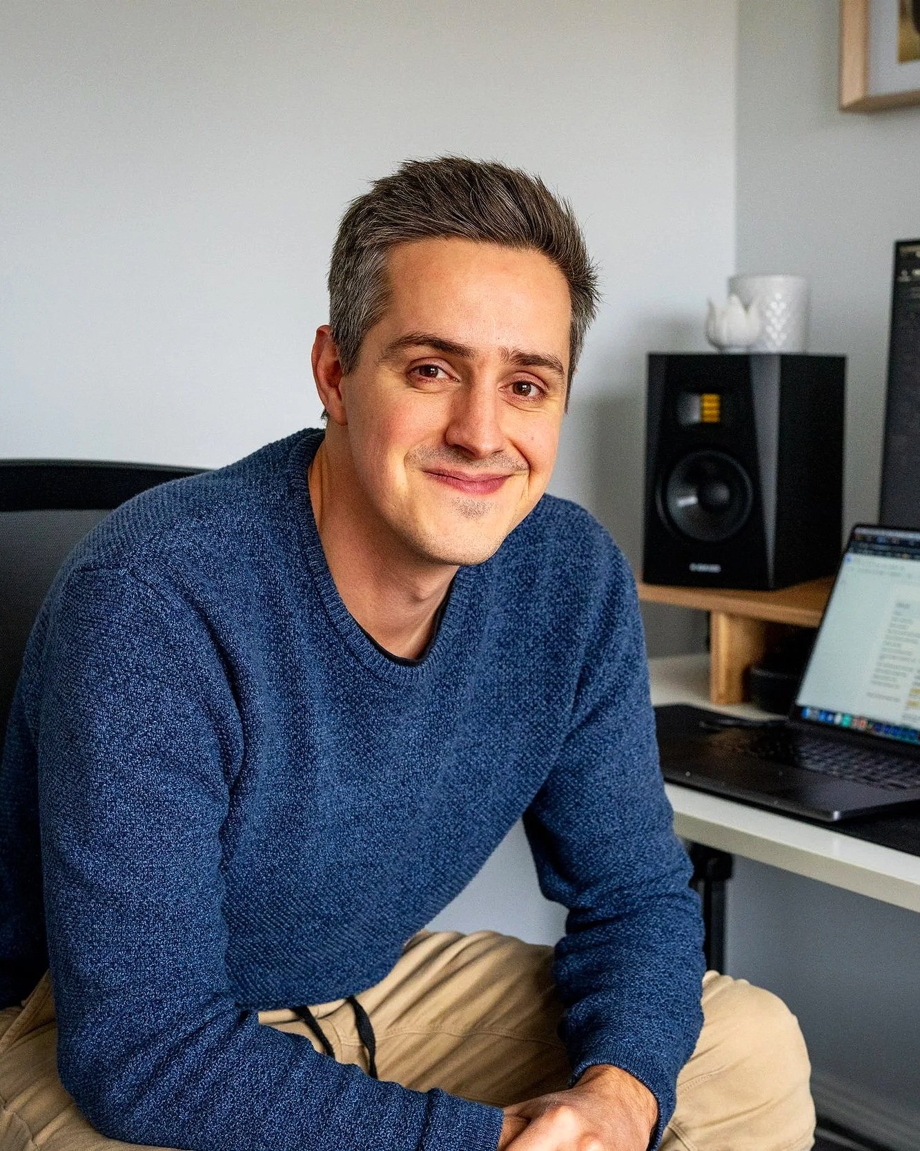 Regan Pearse smiling and sitting in a home office, wearing a blue sweater and beige pants.