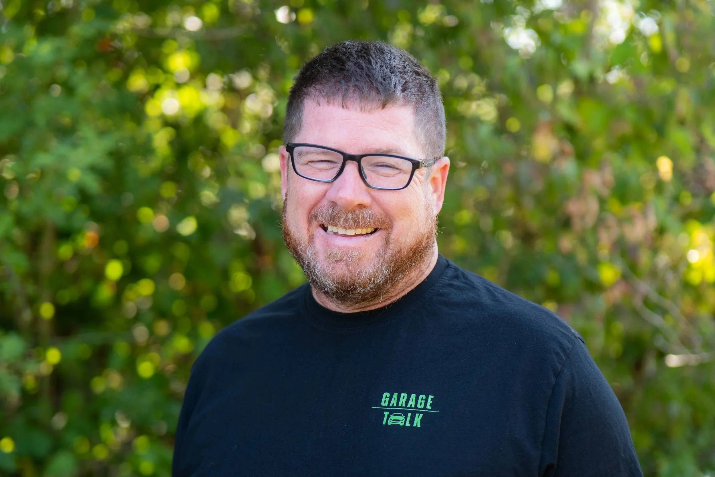 Photo of a man with glasses, short hair, and a beard standing outdoors, smiling