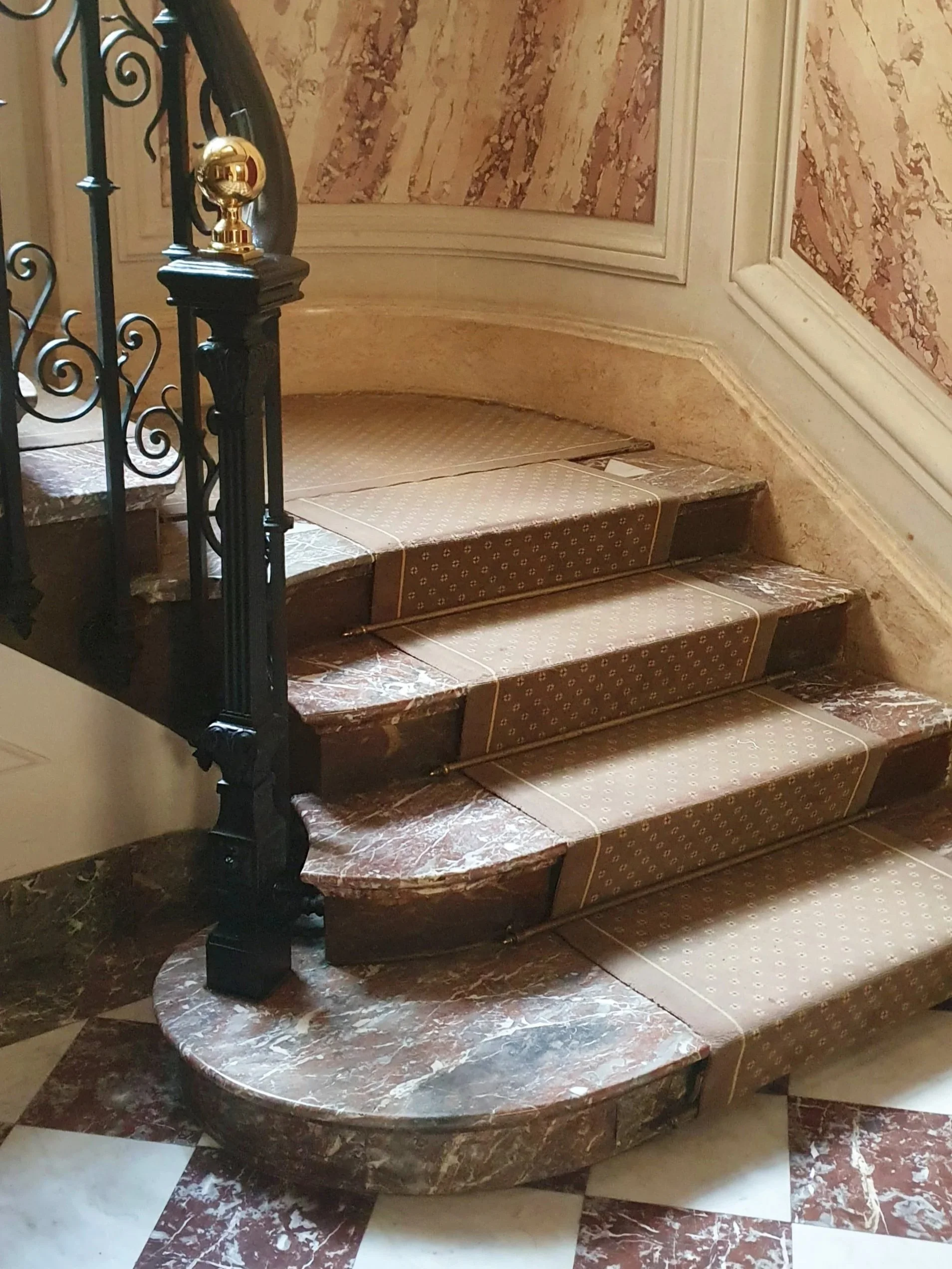 Escalier intérieur en marbre avec tapis beige à motifs, railing en fer forgé et décor mural en stuc