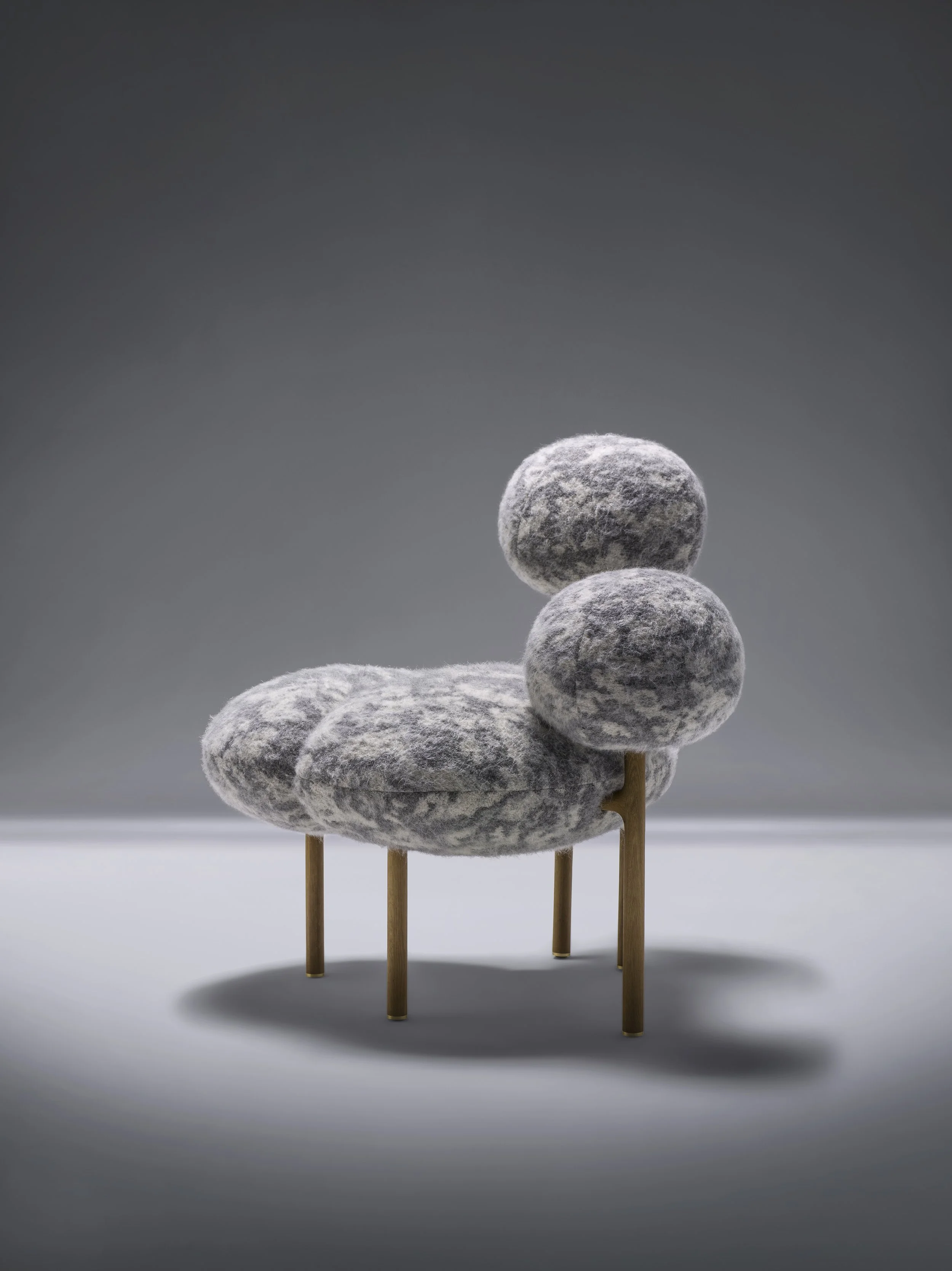 Un fauteuil moderne avec un rembourrage gris en forme de pierres, soutenu par des pieds en bois fins.