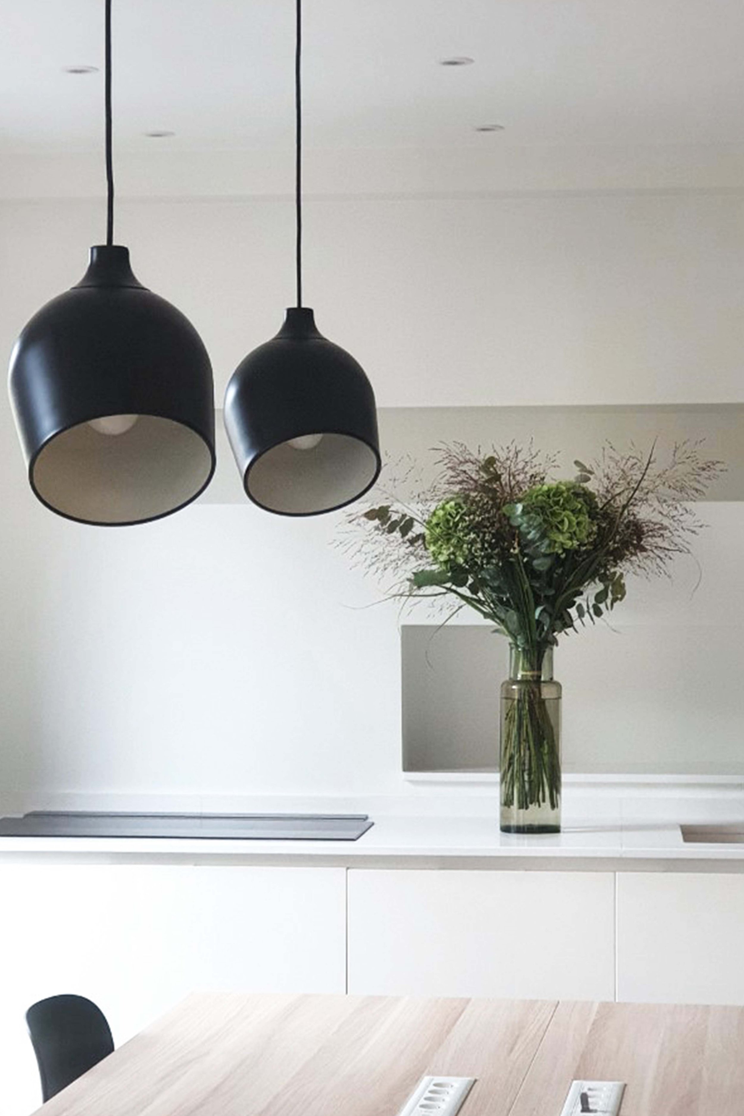 A modern kitchen with two black hanging lamps and a vase with flowers on the worktop.