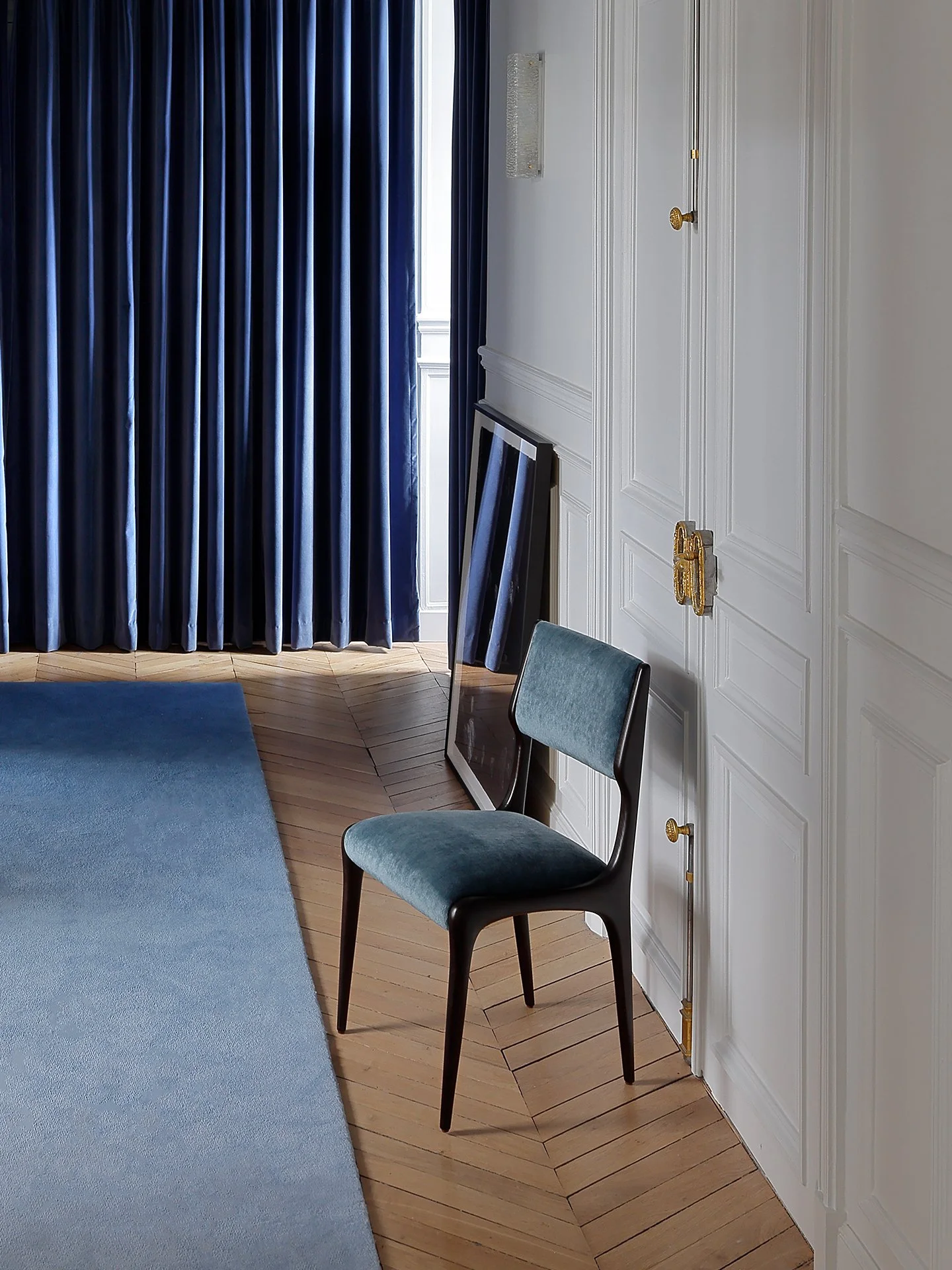 Une chaise avec un coussin bleu dans une pièce avec un mur blanc, un grand miroir et des rideaux bleus.