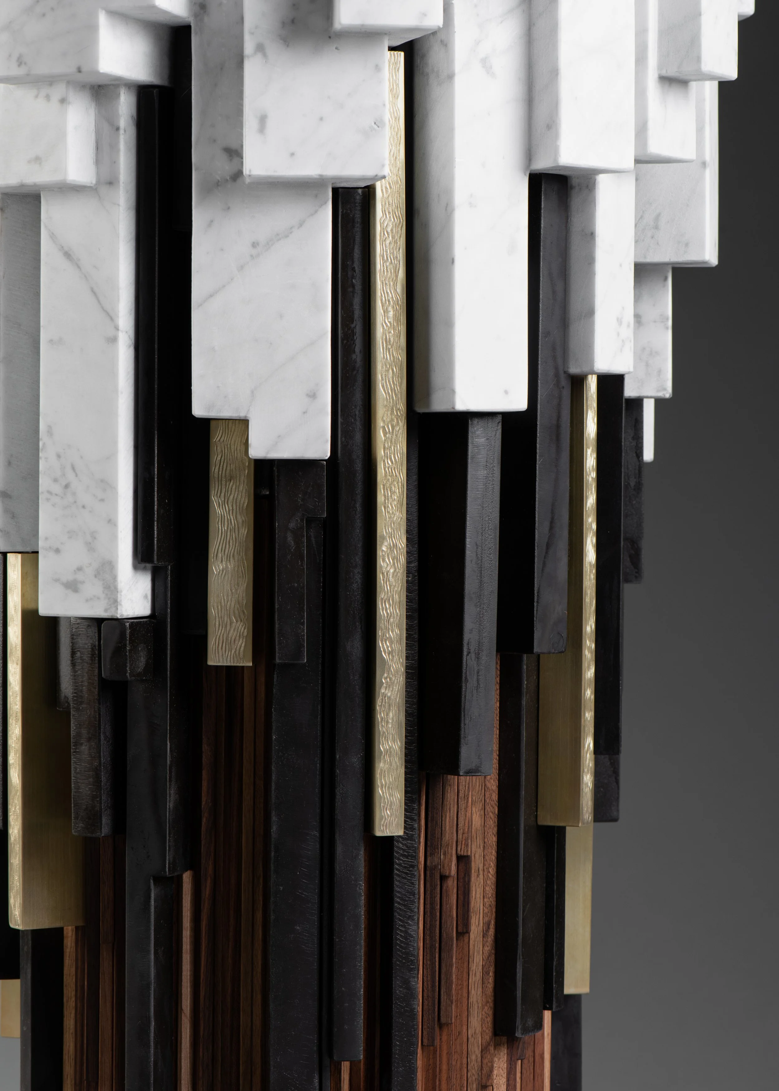 Décor mural composé de blocs en marbre blanc, en bois foncé, en métal noir et en métal doré, formant une composition moderne en relief.