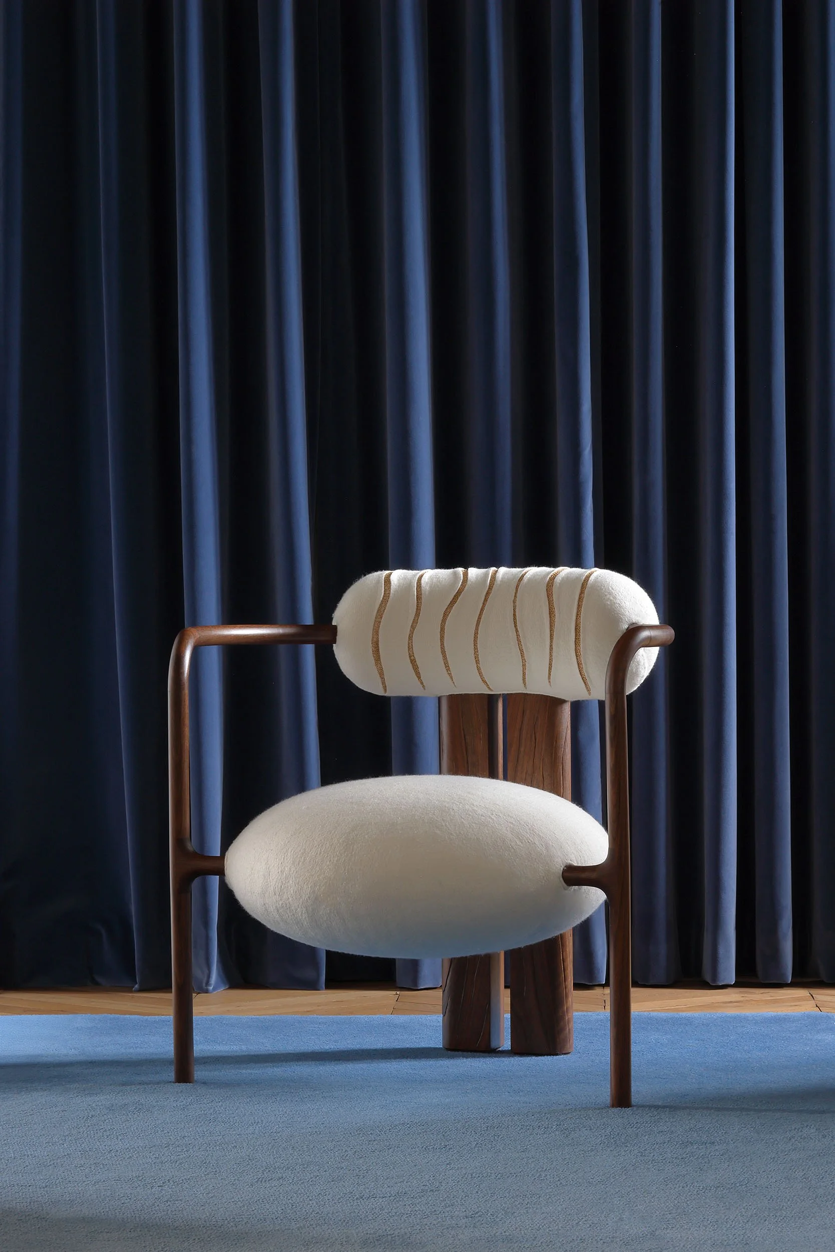 Une chaise moderne en bois avec un rembourrage blanc, placée devant un rideau bleu foncé.