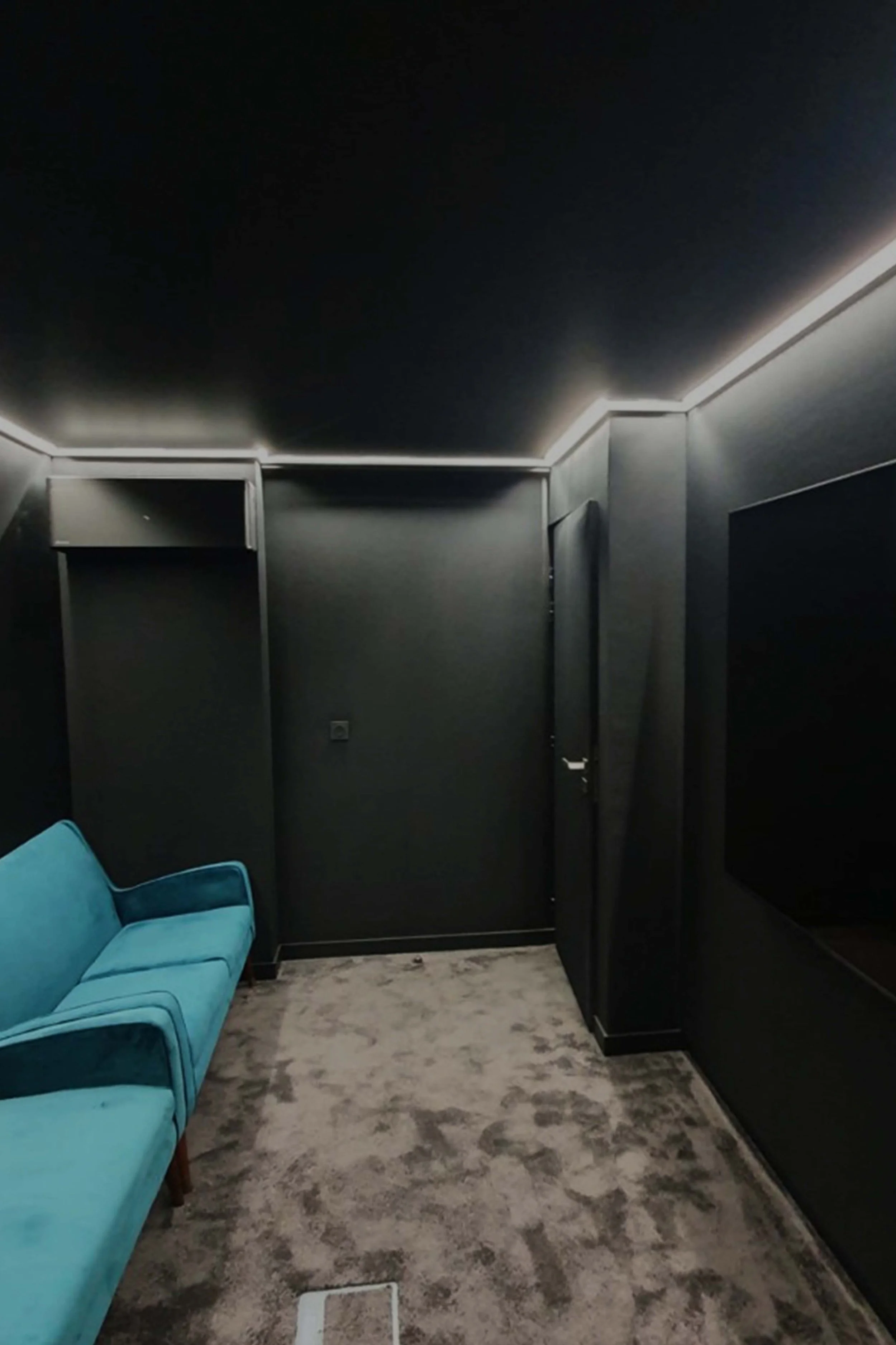 Meeting room or interior lounge with black walls, turquoise sofa, beige carpet floor and white LED ceiling lighting.
