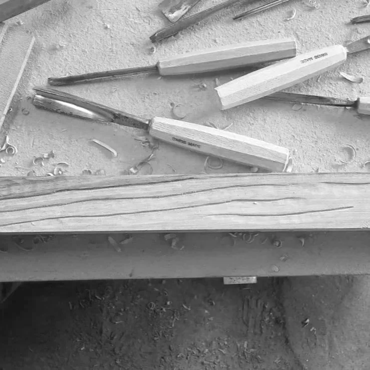 Outils de sculpture en bois, y compris des gouges et des limes, sur une surface en bois avec des copeaux de bois autour.