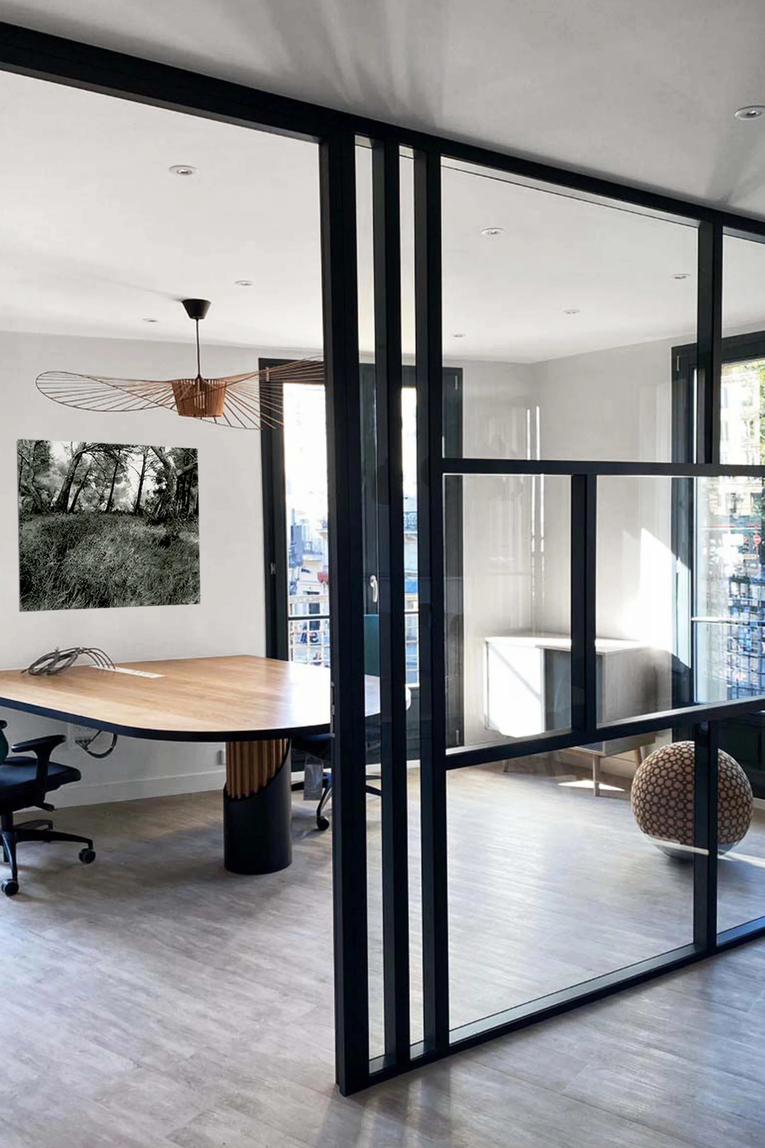 A modern office with a wooden table, desk chair and elegant decorations, separated by a black glass partition.