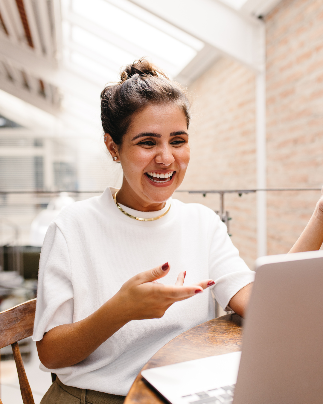 A female business owner smiling, connecting with her business support group, sitting at a wooden table in a bright indoor space