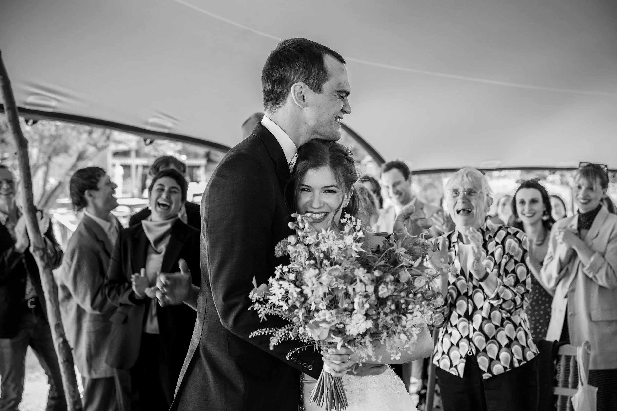Bride smiling in the groom's arms as an older guest claps and cheers after the wedding ceremony in Ireland
