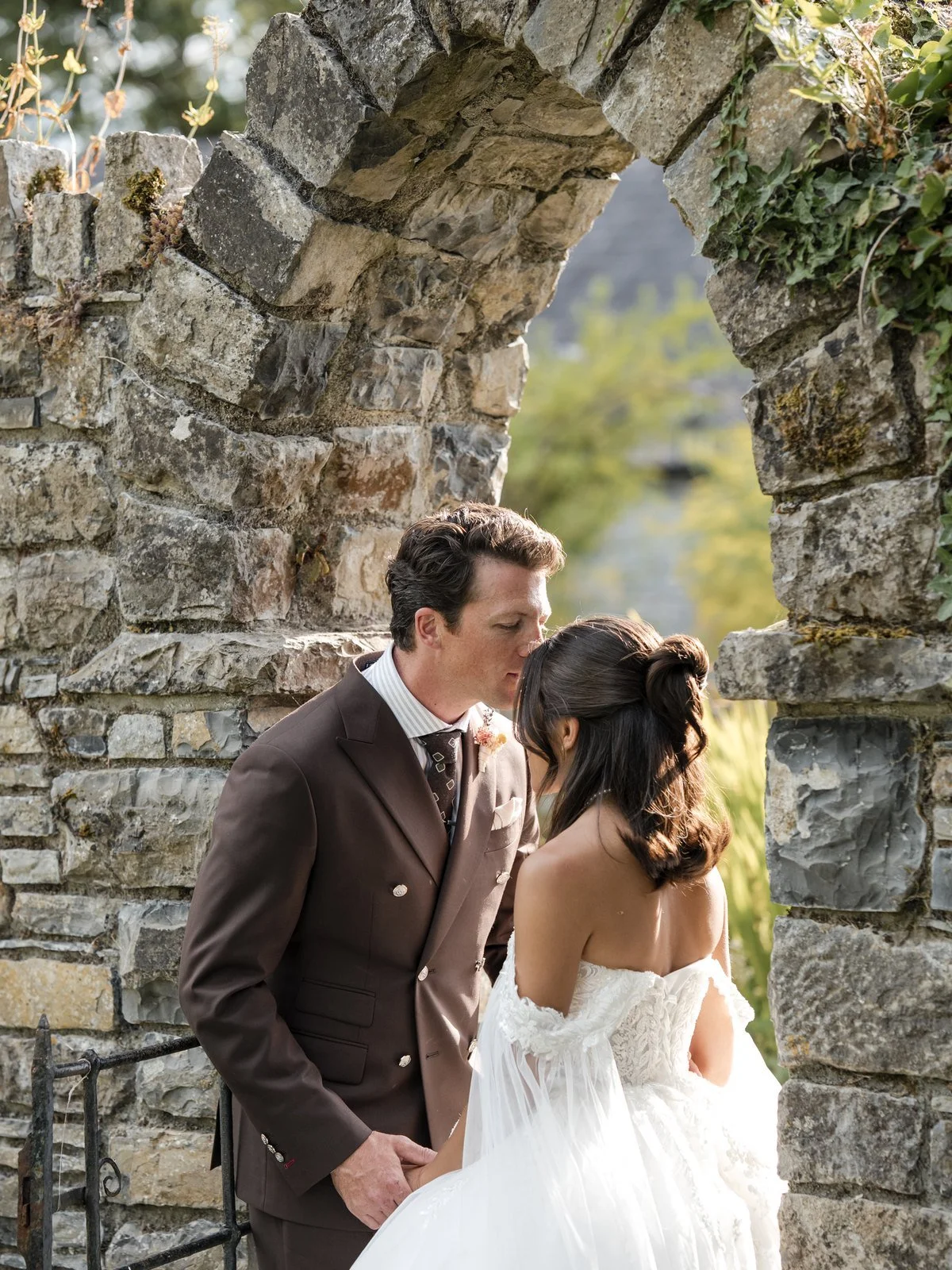 Groom kissing the bride's forehead beneath an old stone arch, Ireland wedding photography