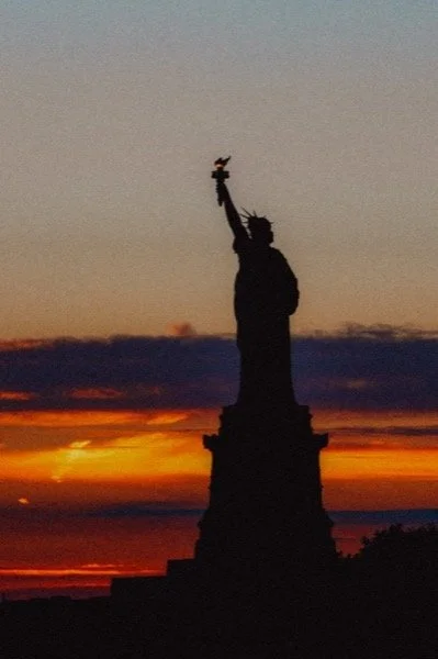 Schattenbild der Freiheitsstatue vor Sonnenuntergang mit orangefarbenem Himmel.