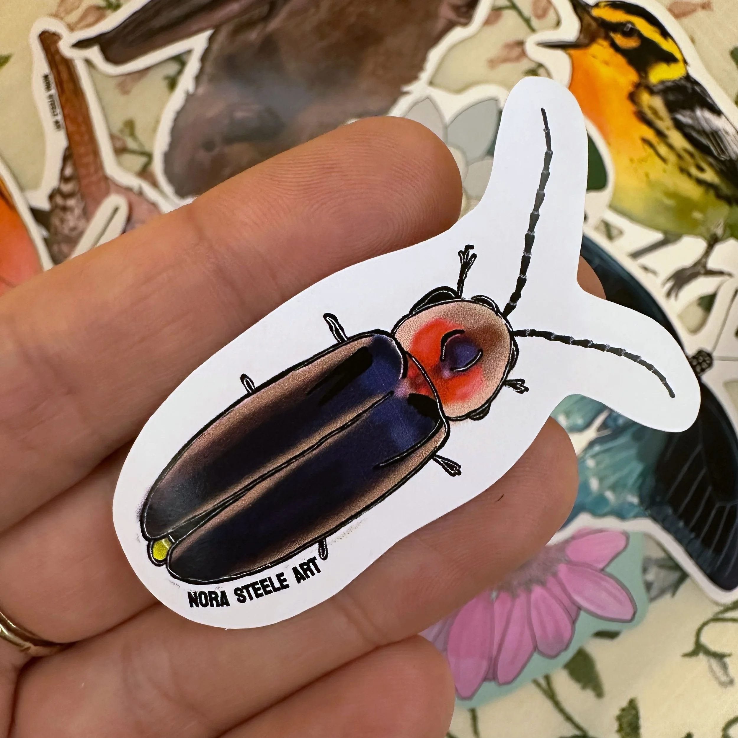 Firefly sticker held above a pile of other stickers