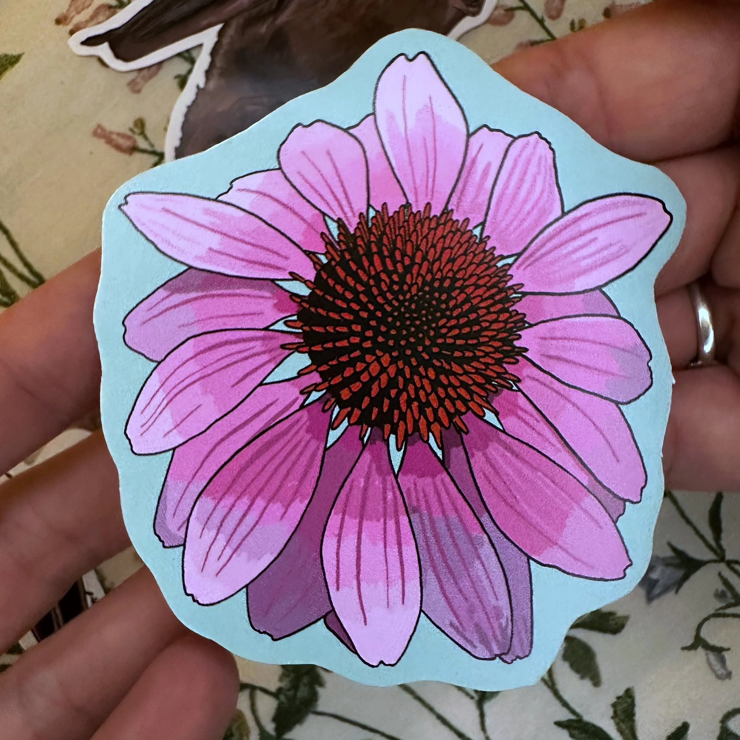 Purple coneflower sticker held above a pile of other stickers