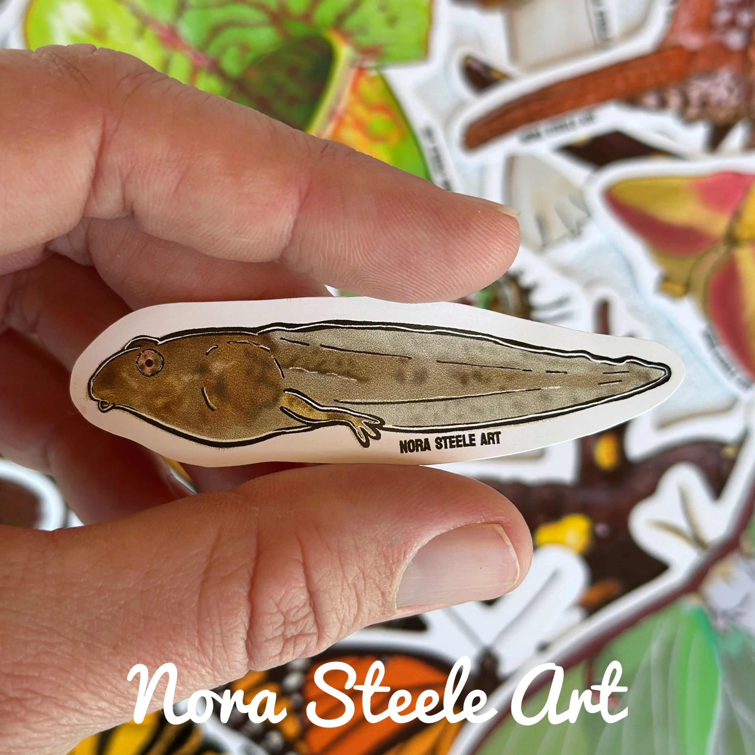 Tadpole sticker held above a pile of other stickers
