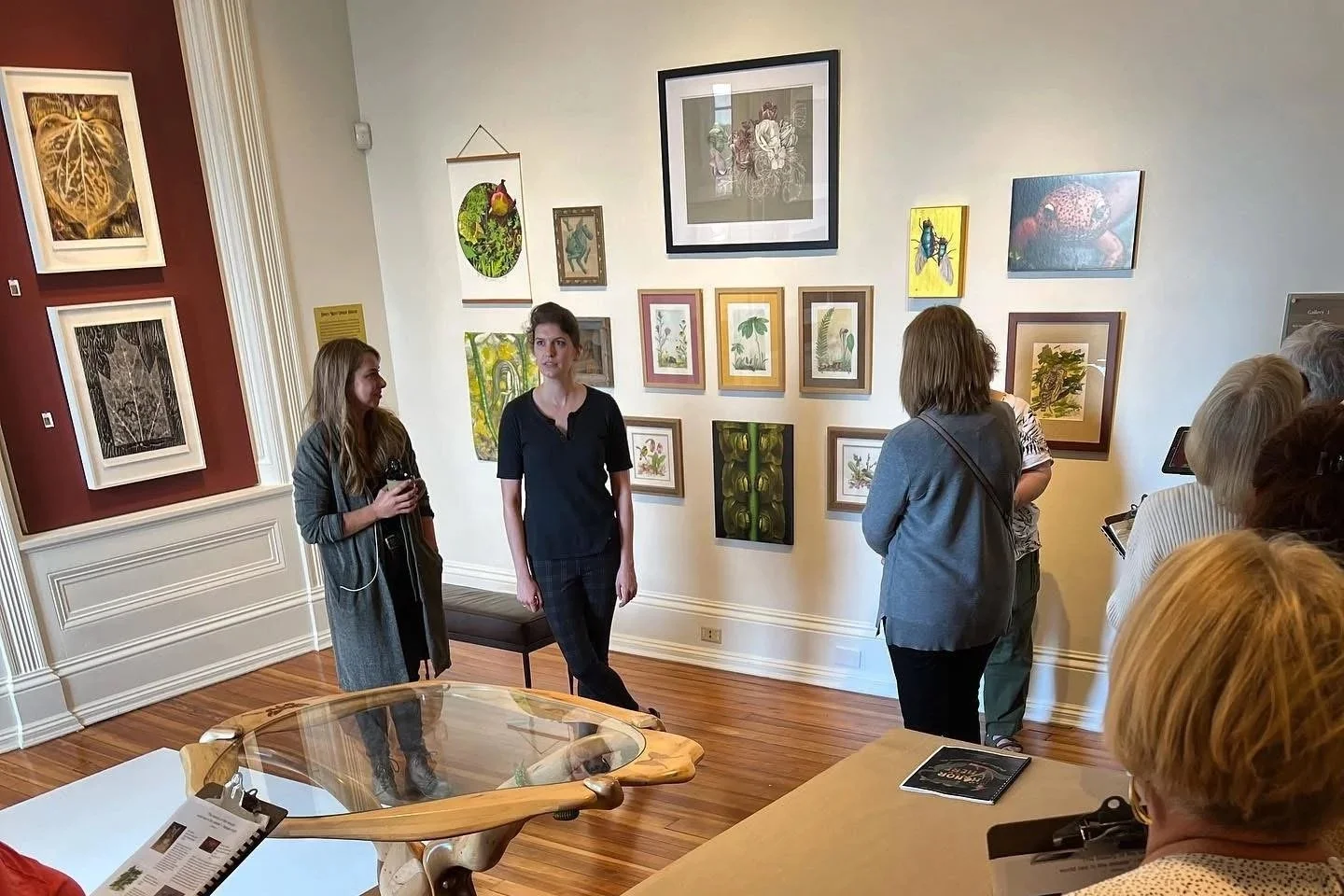 A group of people at an art gallery observing and discussing artwork on the wall.