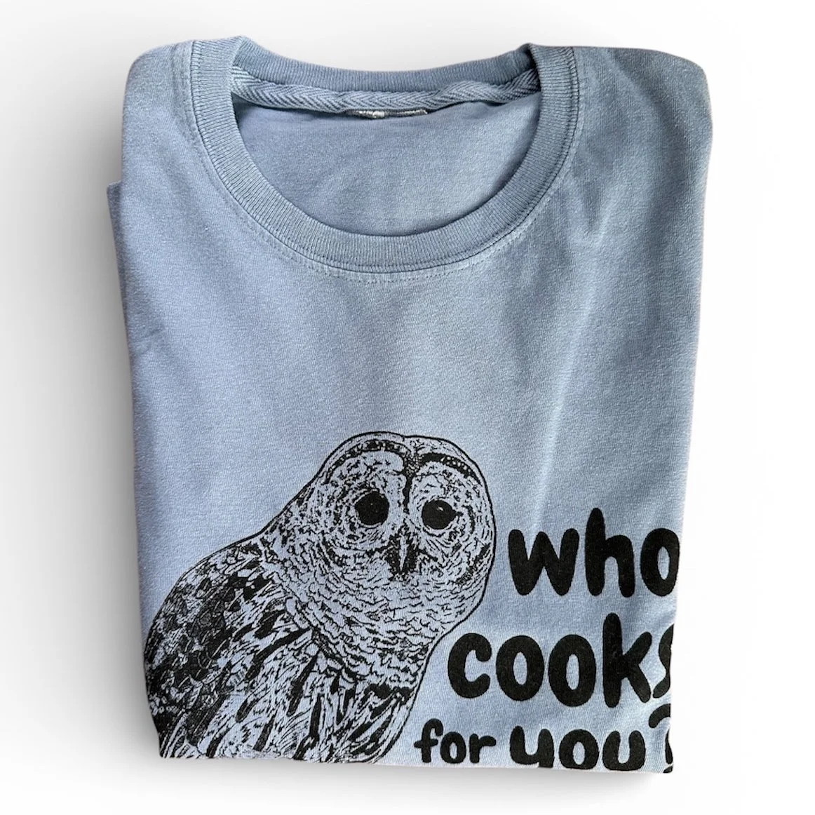 Folded long-sleeve shirt screenprinted with a barred owl and text saying "who cooks for you?"