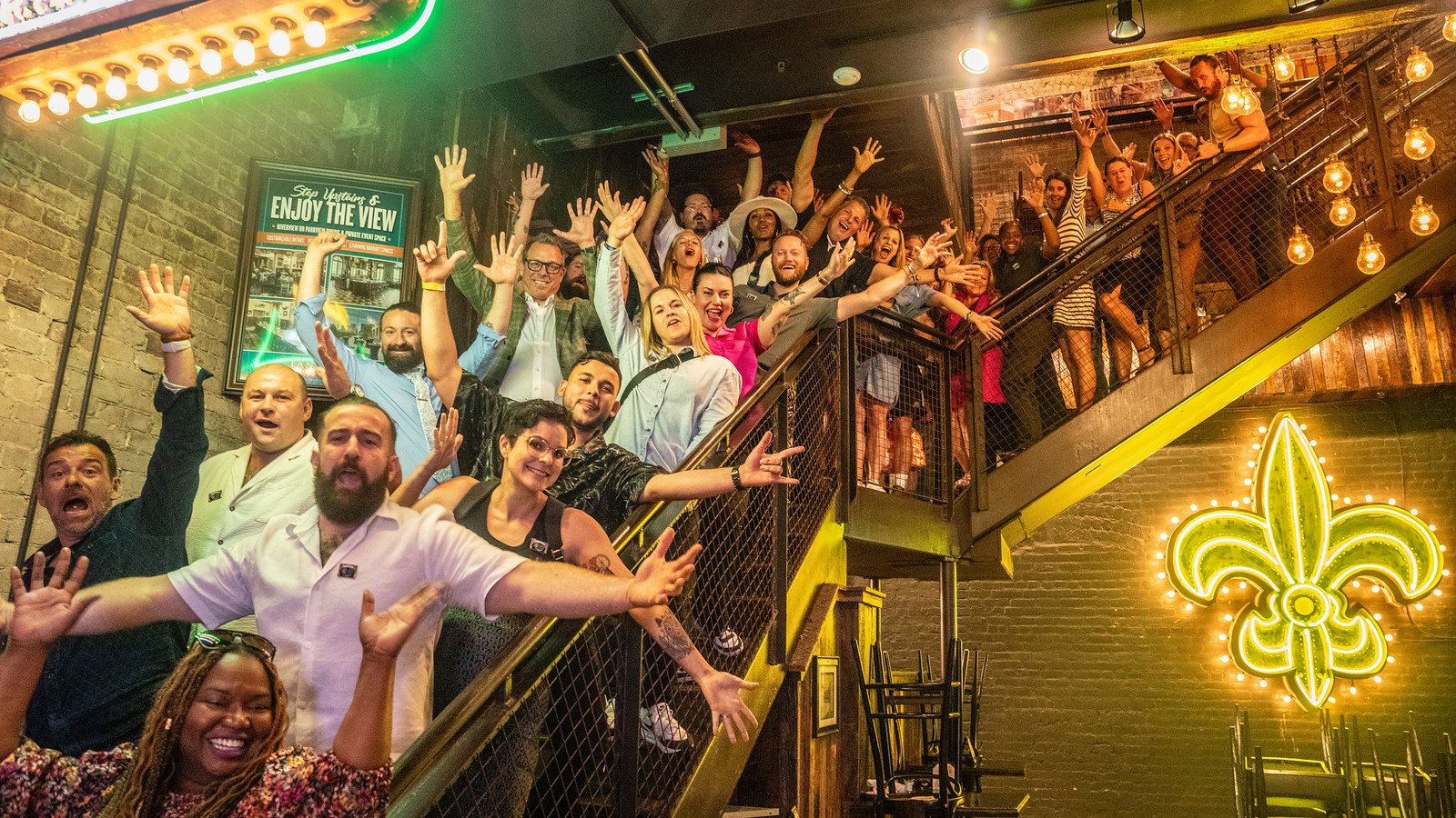 Crowd cheering on a staircase under a neon fleur-de-lis at Marriott's Tales of the Cocktail pop-up in New Orleans