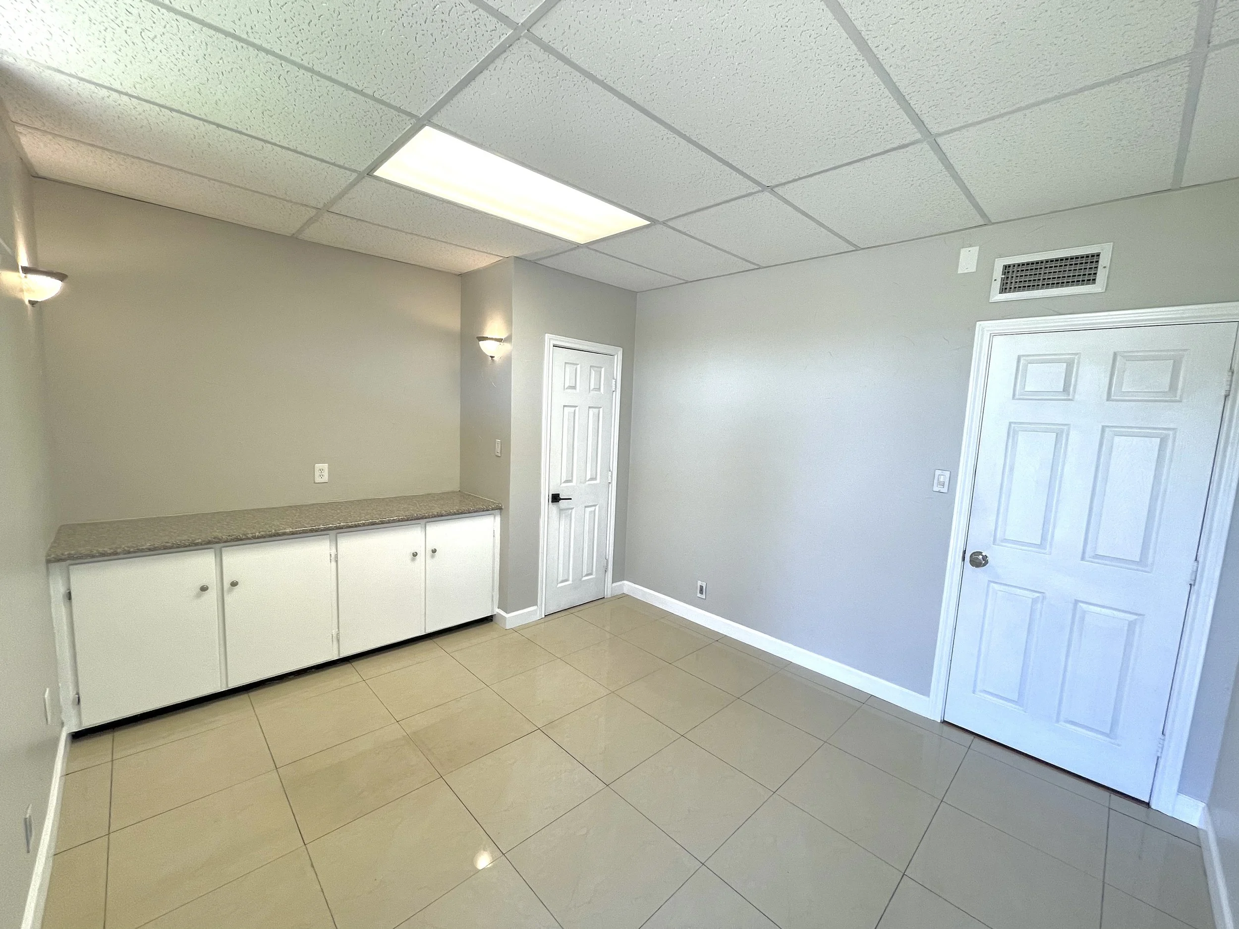 Office kitchenette with light-colored cabinets, countertop, tile flooring, and overhead lighting at 112 W. Pipeline Road in Hurst, Texas.