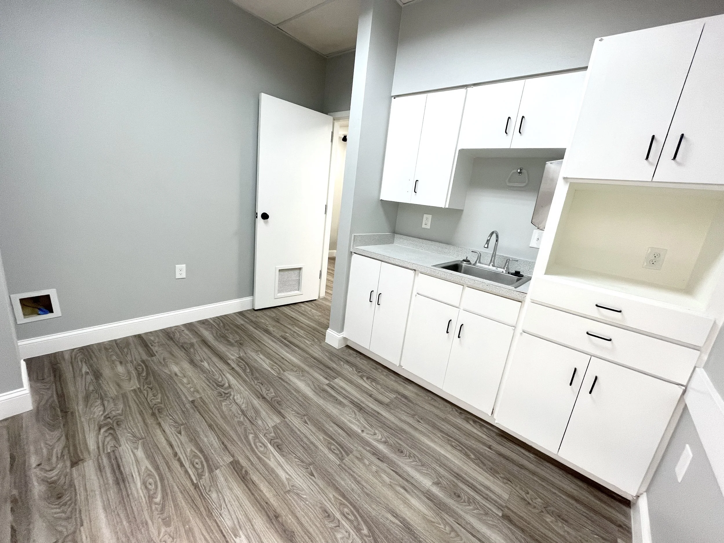 Office kitchenette with white cabinets, sink, and wood-look flooring at 425 Westpark Way in Euless, TX.