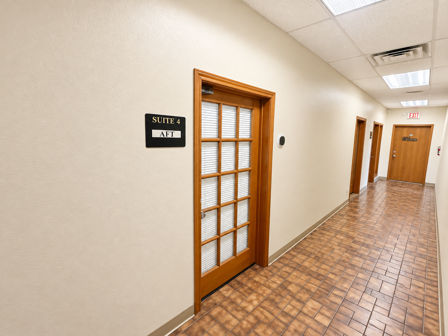 Professional office hallway with wooden-framed glass doors, tile flooring, and overhead lighting at 405 Airport Freeway in Bedford, Texas.