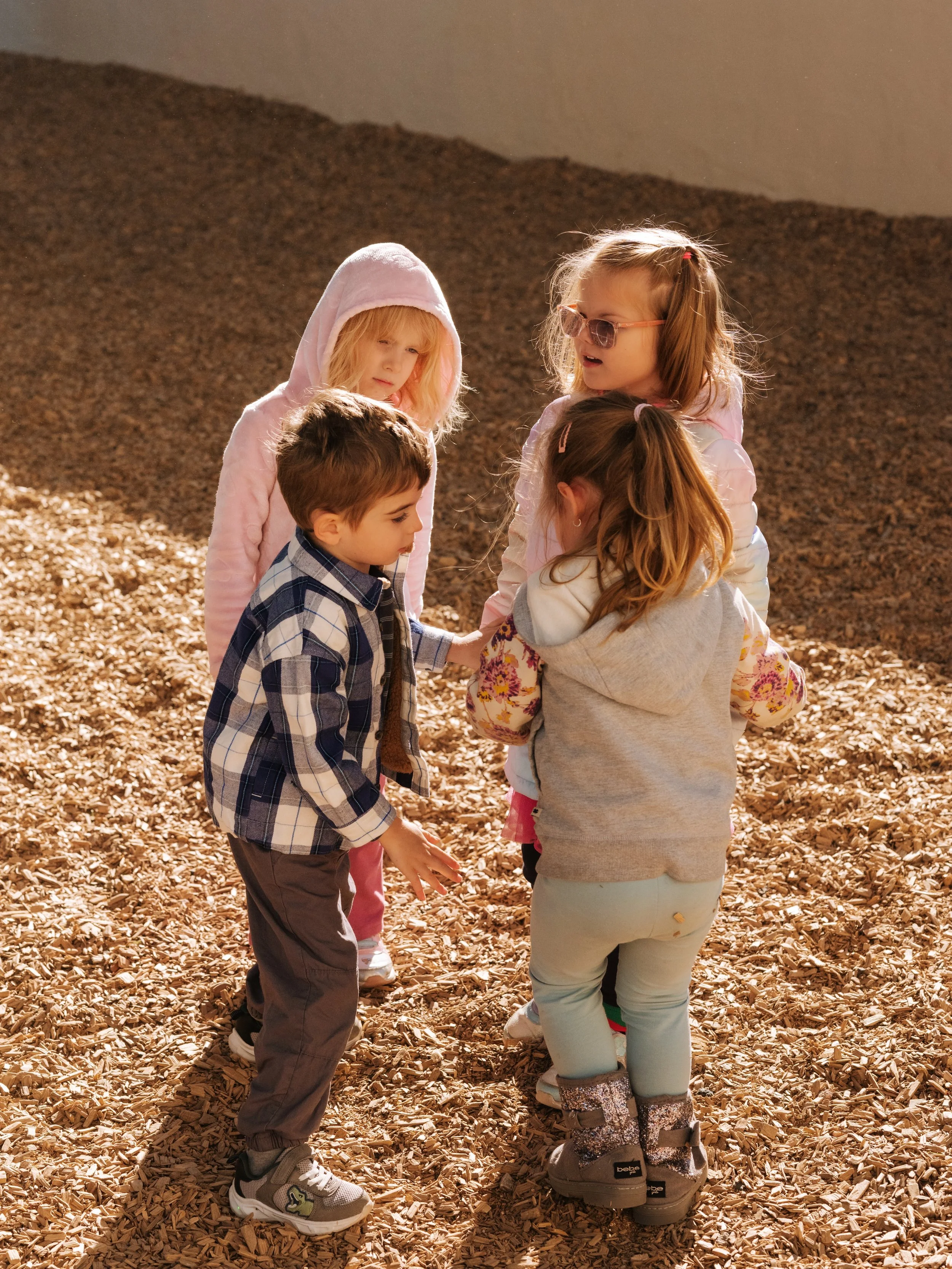 Children in red shirts at a petting zoo, interacting with a large black and red rooster.
