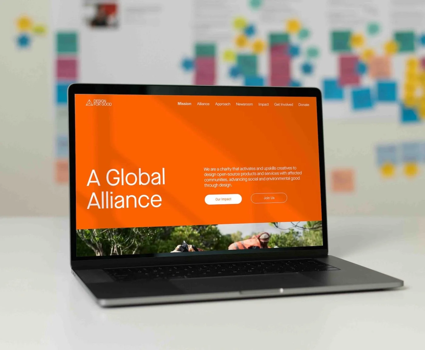 Screenshot of the homepage for 'Design for Good' charity website featuring a navigation menu, an orange banner with mission statement, a call-to-action button, and a photograph of people working in a green field.