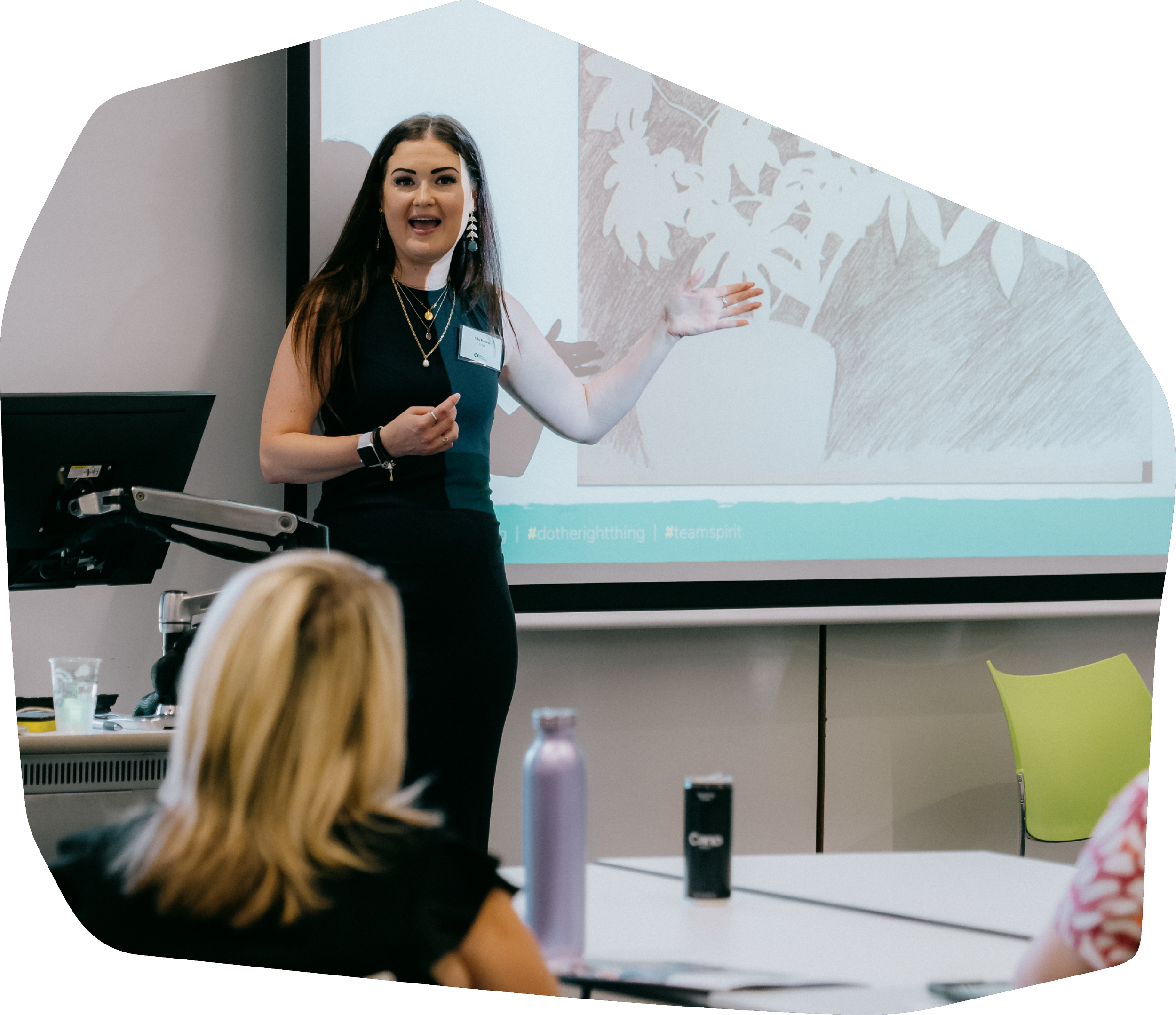 A woman giving a presentation in a conference room, standing next to a projected slide showing a drawing of a tree.