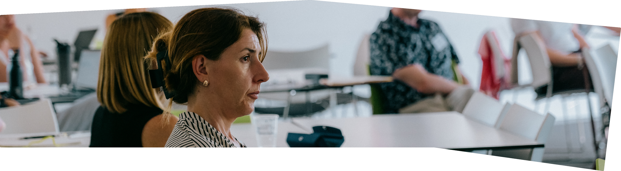 A woman with short brown hair, wearing a striped shirt, attending a class or seminar in a classroom setting.